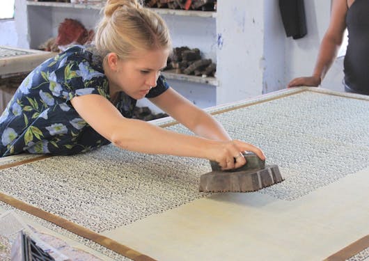 An adult female white traveler uses a block printer at an artisan visit in India.