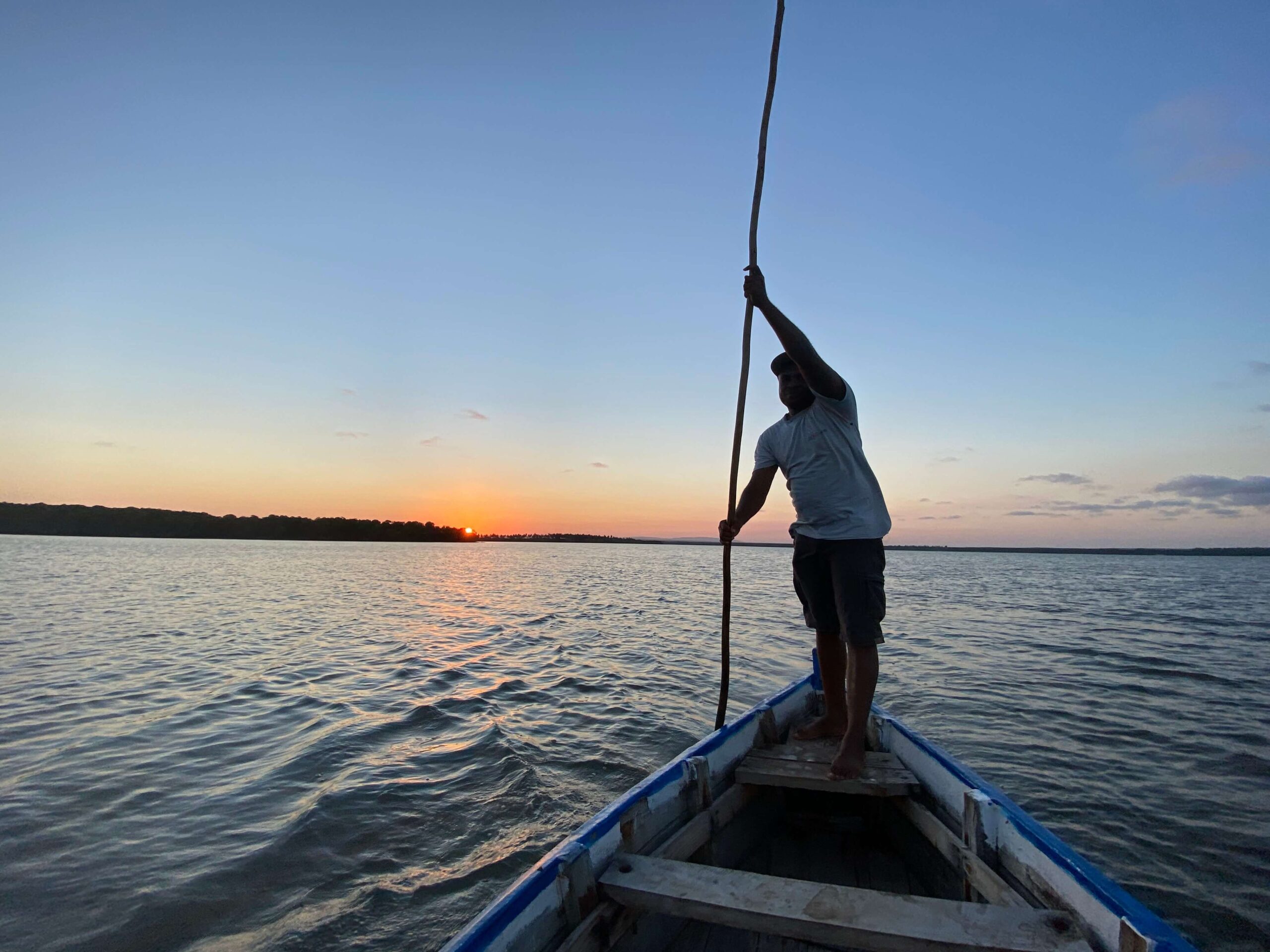 A local Kenyan man paddles a canoe at sunset.