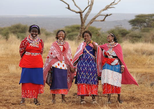 A group of four Maasai Mara women smile and pose for a photo wearing traditional attire.