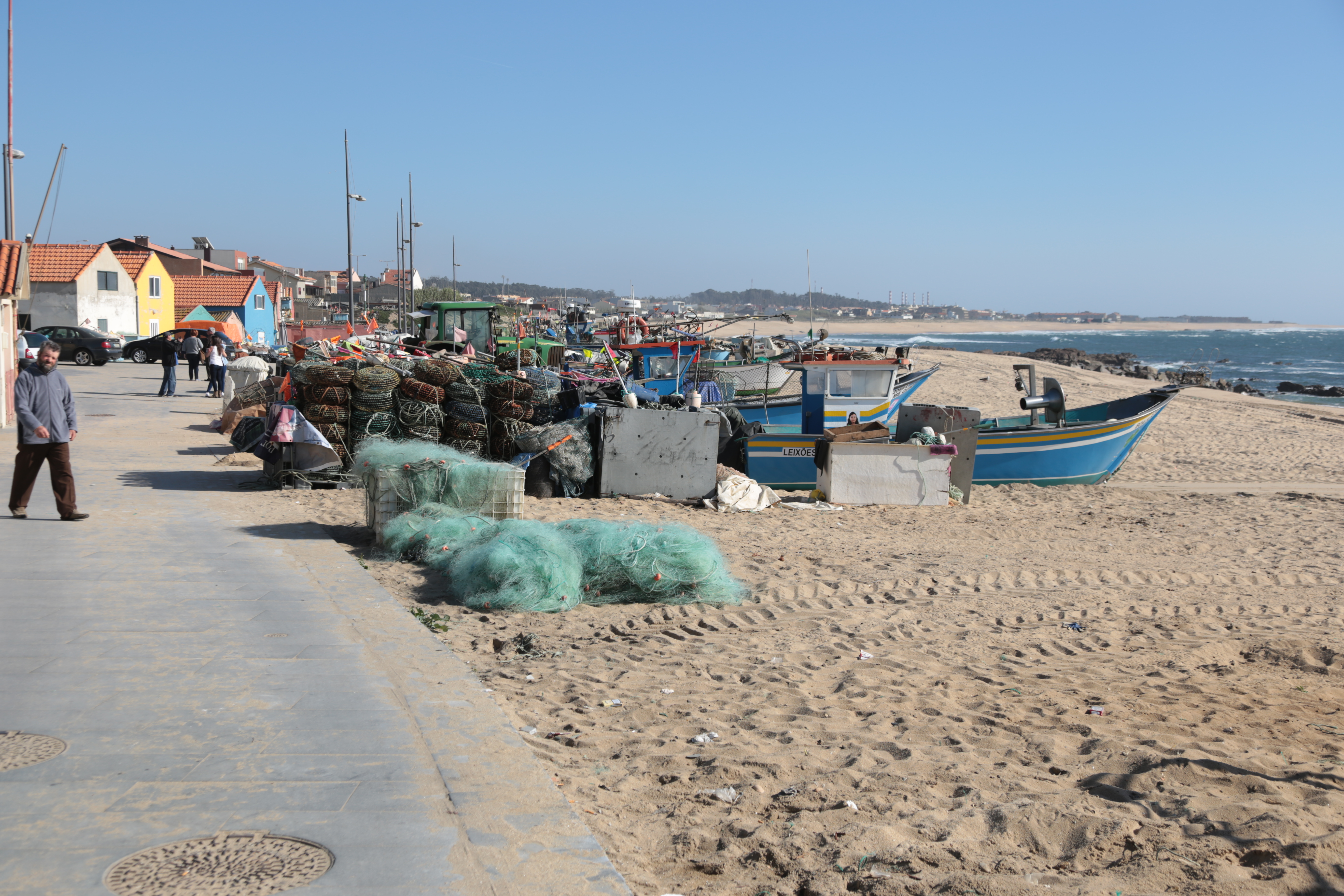 A seaside town in Portugal is shown with sand and fishing boats on the shore.