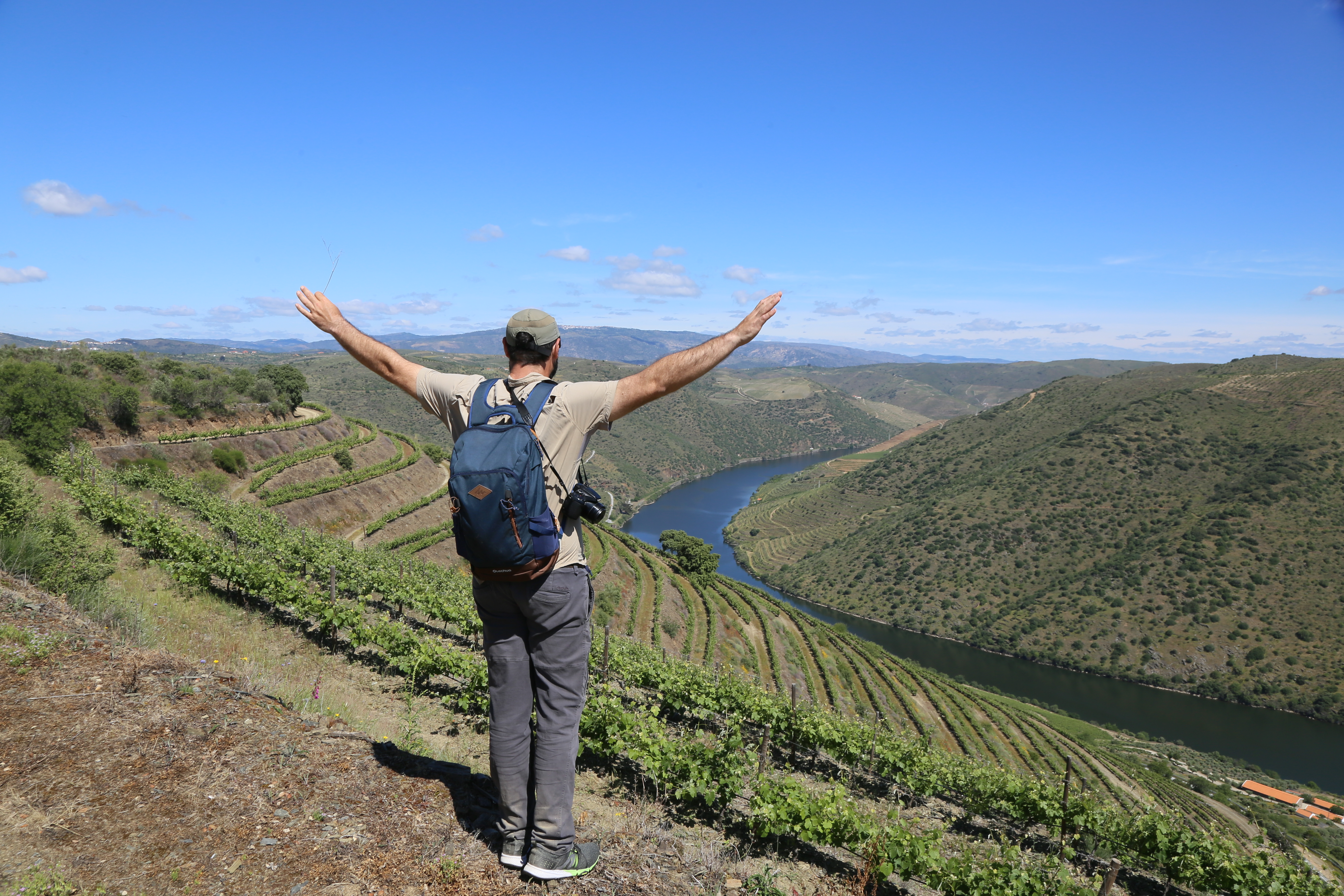 A walker stops to admire the Douro Valley in Portugal, with vineyards below and the Douro River cutting through the valley.