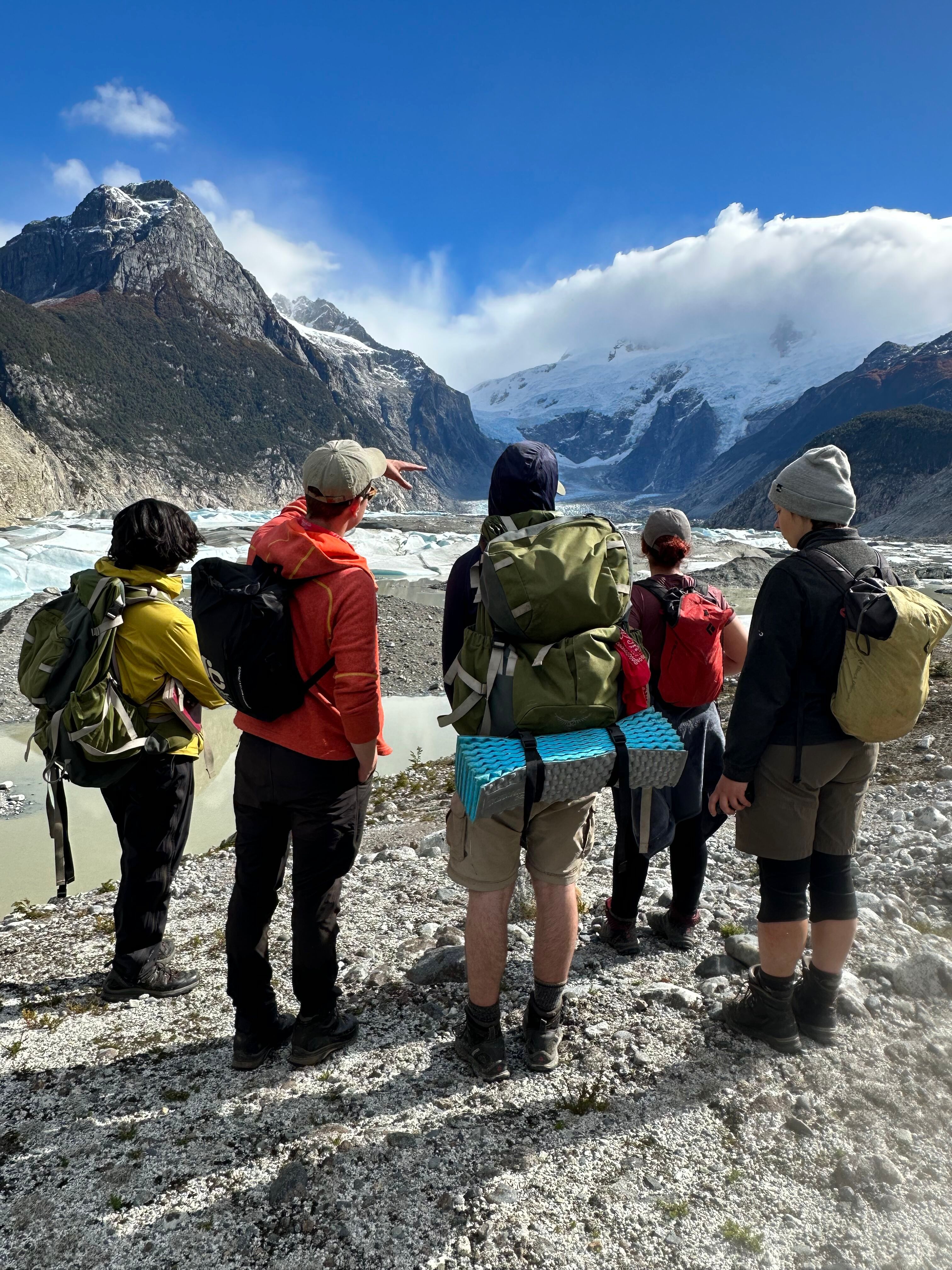 A group of 5 trekkers stand on a sunny ridge and look out over a mountain peak.