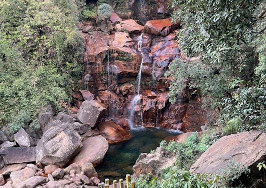 A waterfall cascading over reddish rocks with a walkway leading up to it, shown in Cherrapunjee, Meghalaya, India.