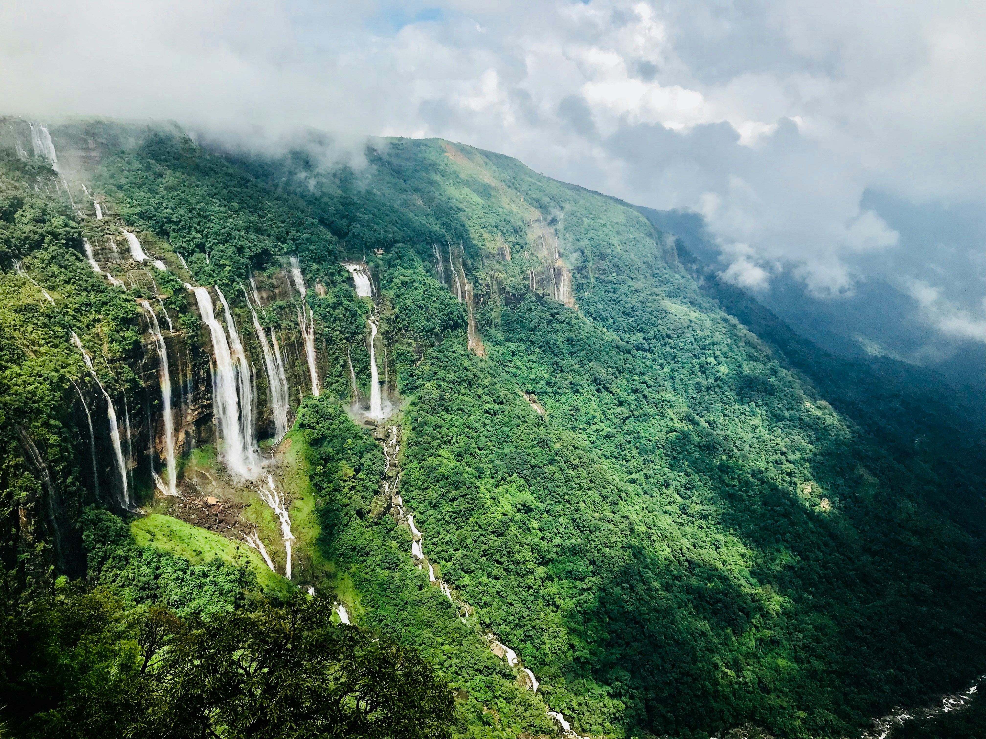 The Seven Sister Falls are shown in Shillong, Meghalaya, India - a stunning set of waterfalls cascading over a green hillside.