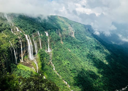 The Seven Sister Falls are shown in Shillong, Meghalaya, India - a stunning set of waterfalls cascading over a green hillside.