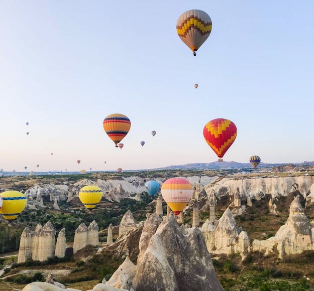 Colorful hot air balloons in Cappadocia, Turkey, take to the sky in the early morning above pale white Fairy Chimney volcanic rocks.