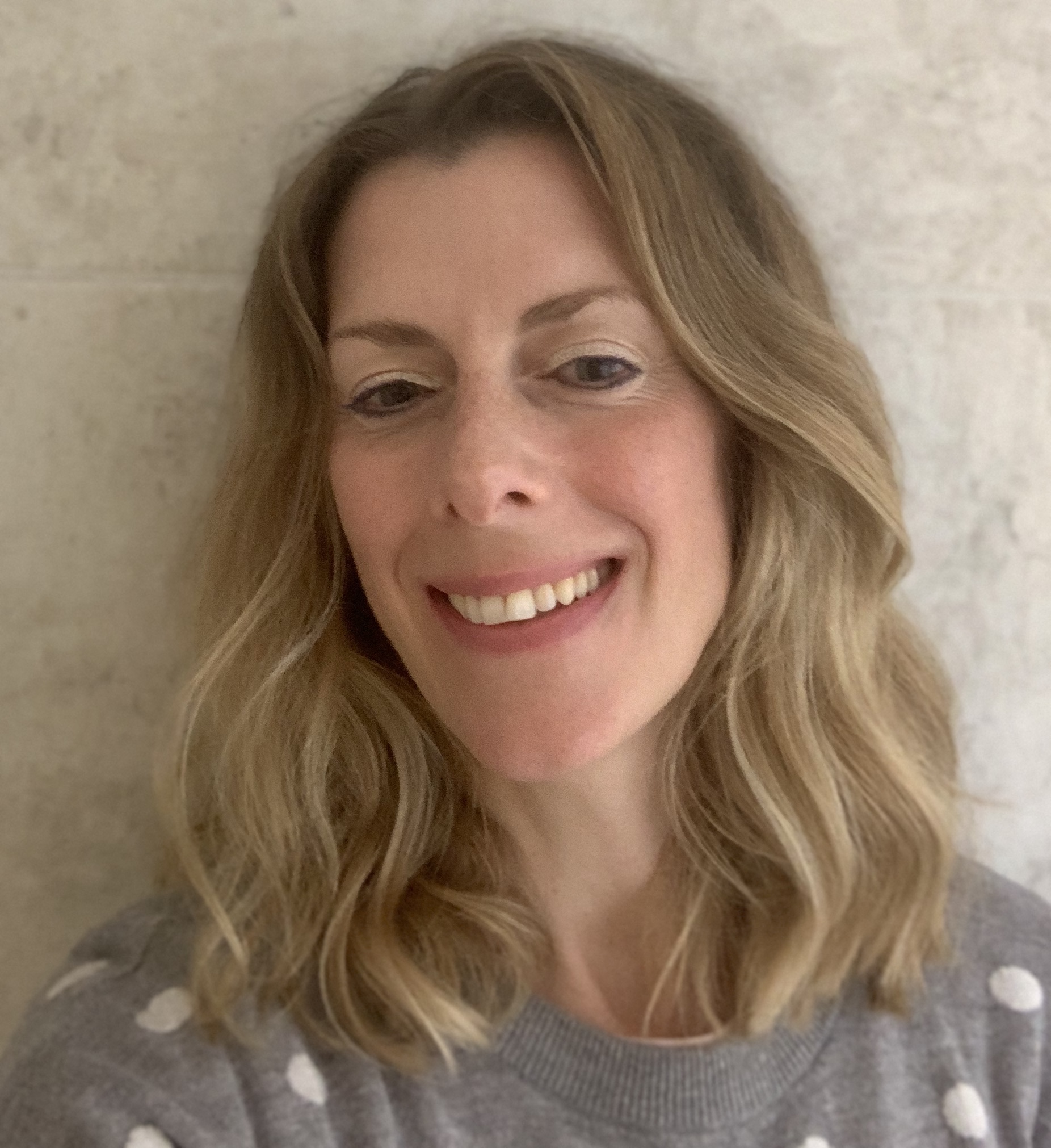 A headshot of a young Caucasian woman with shoulder-length, wavy, blonde hair smiling at the camera.