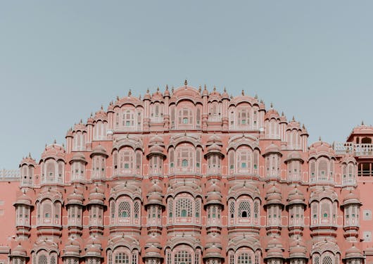 The Hawa Mahal, or Pink Palace, majestically sits in the center of the frame with a hazy blue sky above and behind it. This famous and ornate palace is in Jaipur, India, and can be seen on the Golden Triangle Cultural Tour.