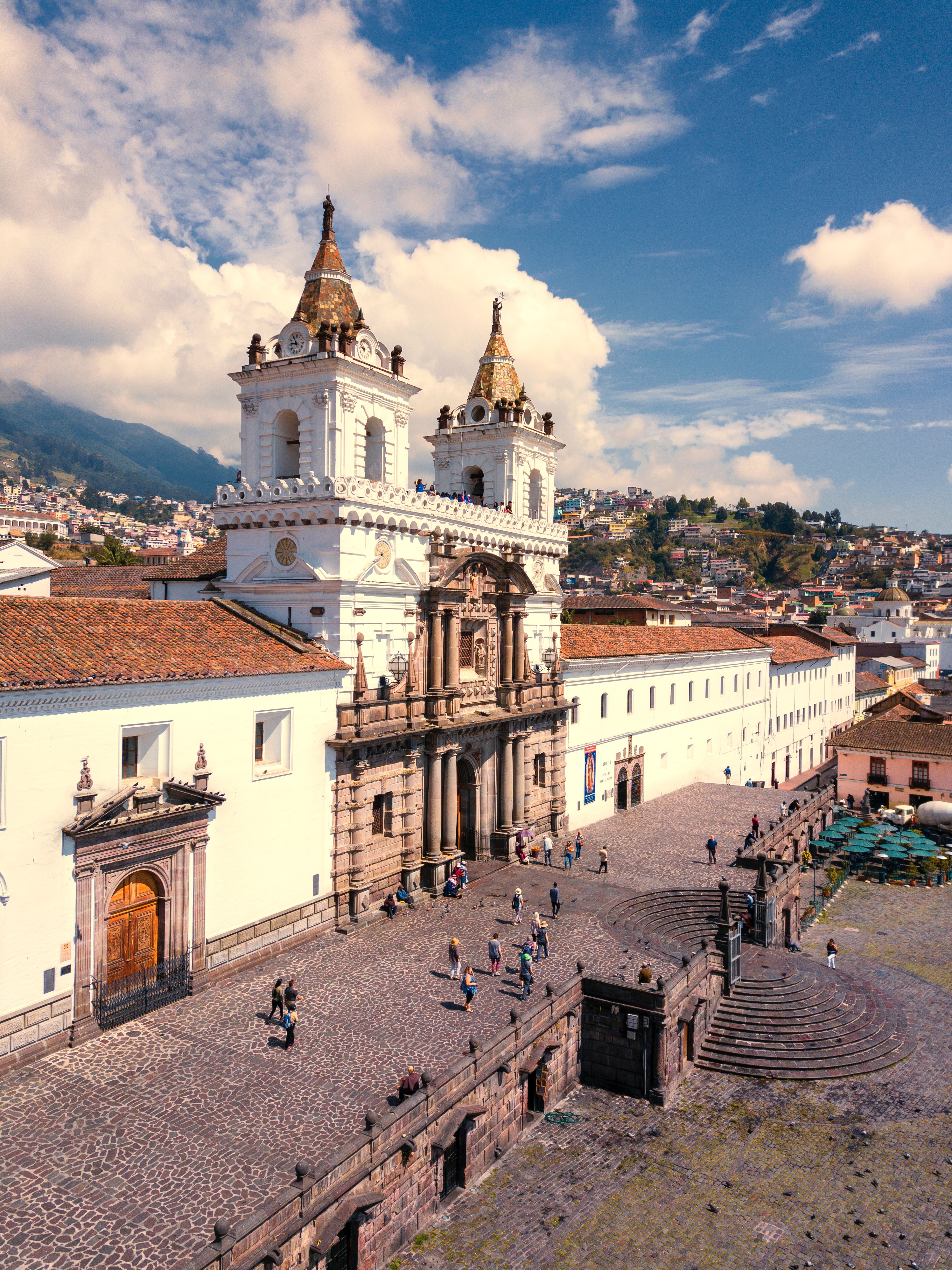 An aerial view of the famous San Francisco cathedral in Quito, Ecuador stands against a blue, cloudy sky.