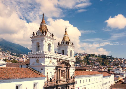 An aerial view of the famous San Francisco cathedral in Quito, Ecuador stands against a blue, cloudy sky.