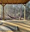 An open air yoga shala in the woods in Portugal sits empty in afternoon sunlight streaking through tres, with black yoga mats rolled out waiting for students. Two red hammocks are hanging in the distance.