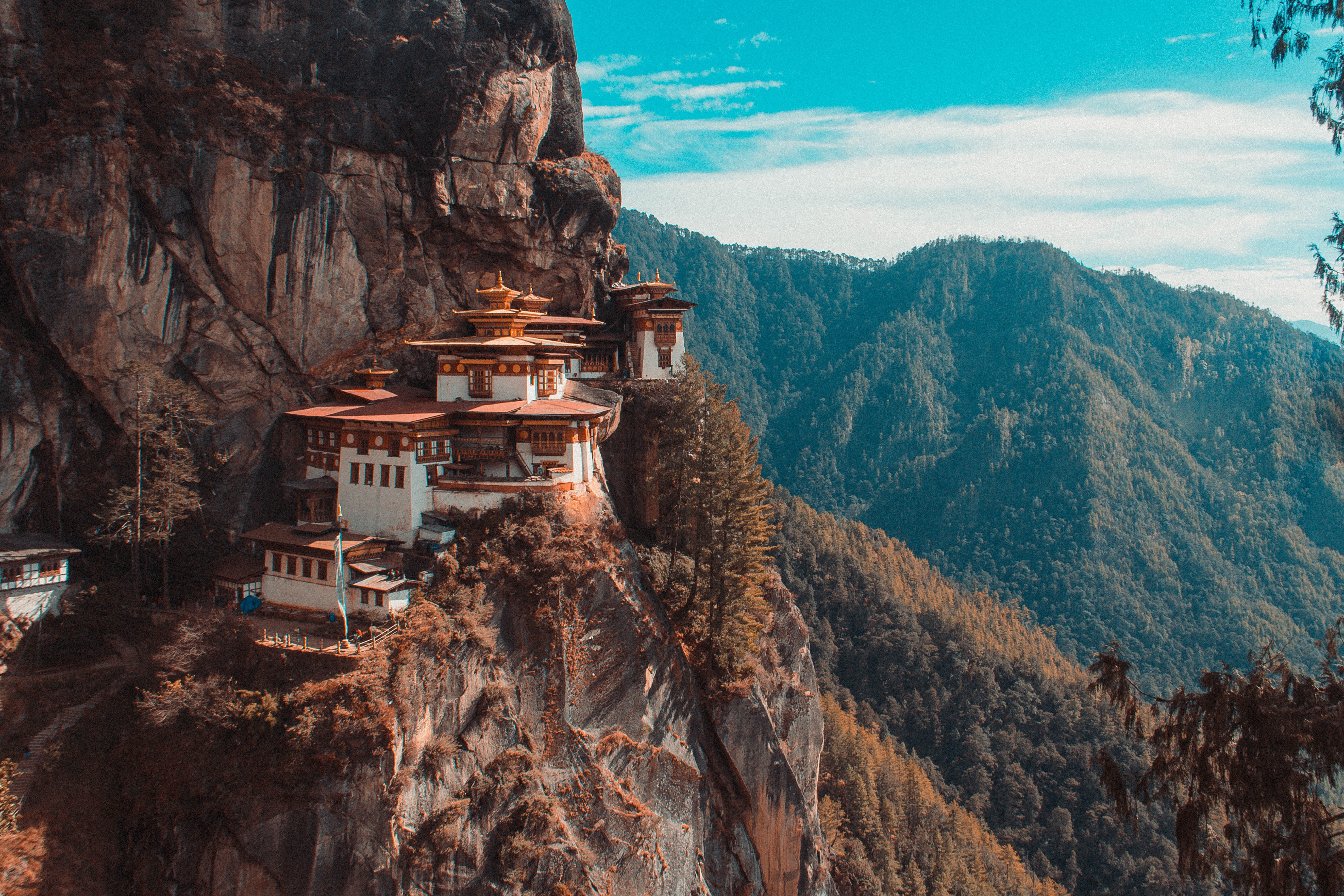 The iconic Tiger's Nest Monastery near Paro, Bhutan sits nestled amongst steep cliffs, with forest in the background and a blue sky overhead.