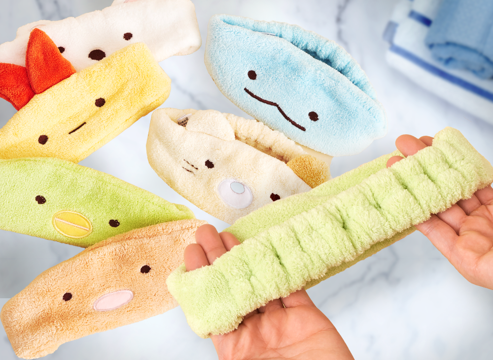 Sumikko Gurashi hair bands on top of a white counter top with a hand holding the green Penguin? hairband up to the camera