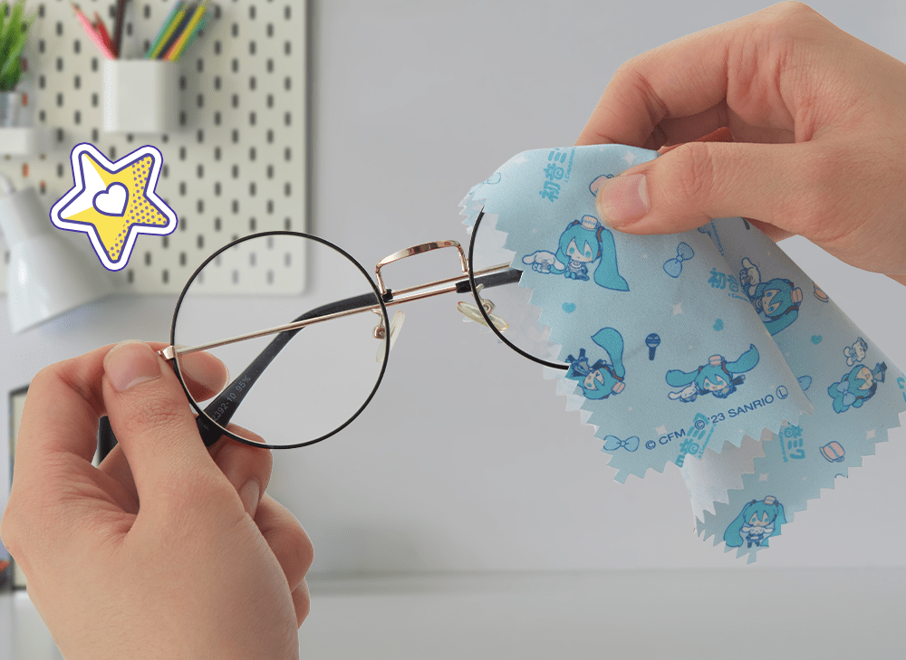 A picture of hands holding a pair of glasses while cleaning one of the lenses with a Hatsune Miku and Cinnamoroll microfiber cloth.