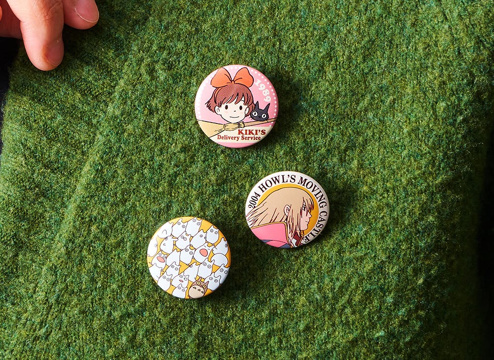 Three Studio Ghibli badges on a green sweater feature Totoro, Kiki, and Howl 