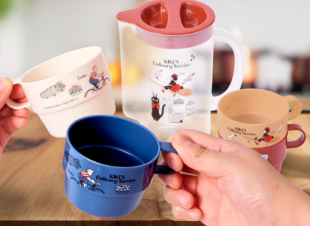 A hand holding the blue Kiki's Delivery Sice cup in front of the Kiki's Delivery Service pitcher