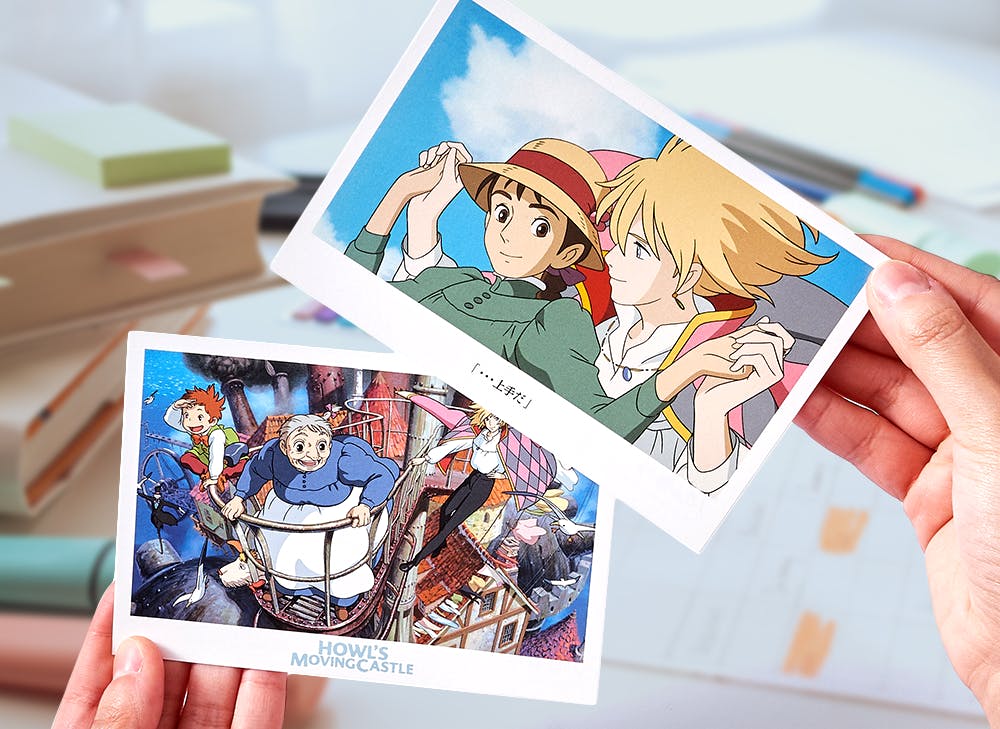 Hands holding up two postcards featuring scenes from Howl's Moving Castle 
