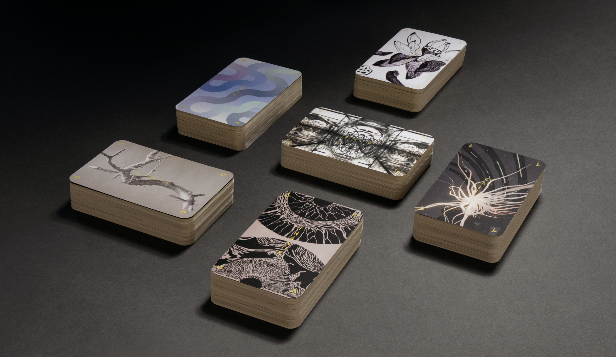 Photo showing six stacks of cards face up on top of a dark gray seamless. They are arranged neatly and the top cards showing are all in shades of grays, blues, and lavender.