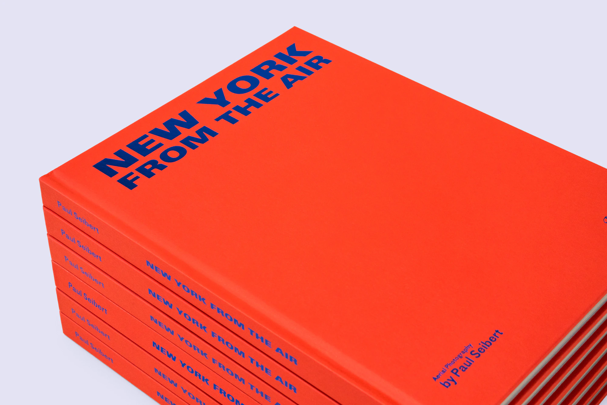 A photo showing a stack of the NEW YORK FROM THE AIR books. The books are red with the title in cobalt blue foil. The stack is standing on a light gray seamless.