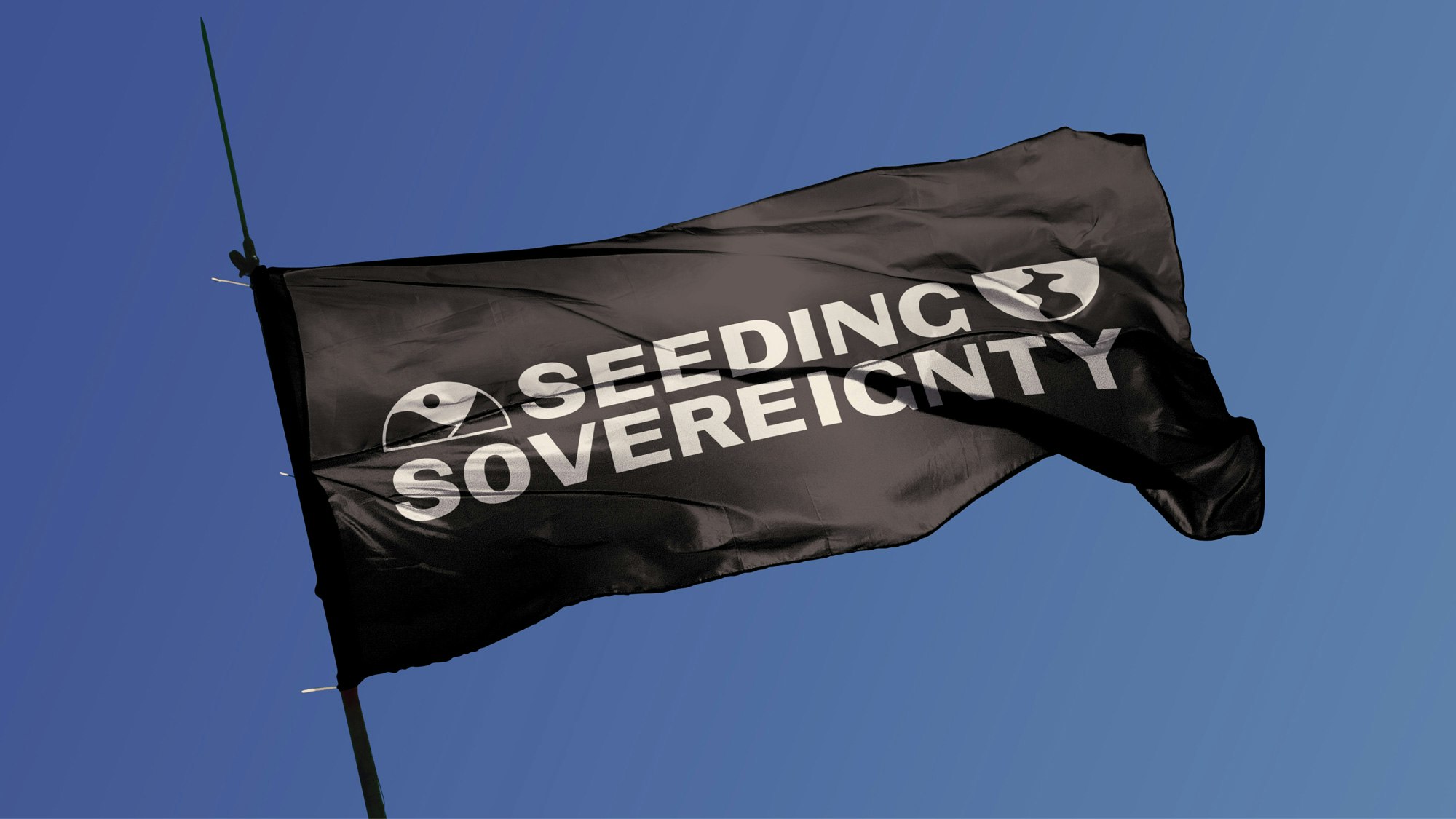 Image shows a black flag against a blue sky with the Seeding Sovereignty logo on it in white.