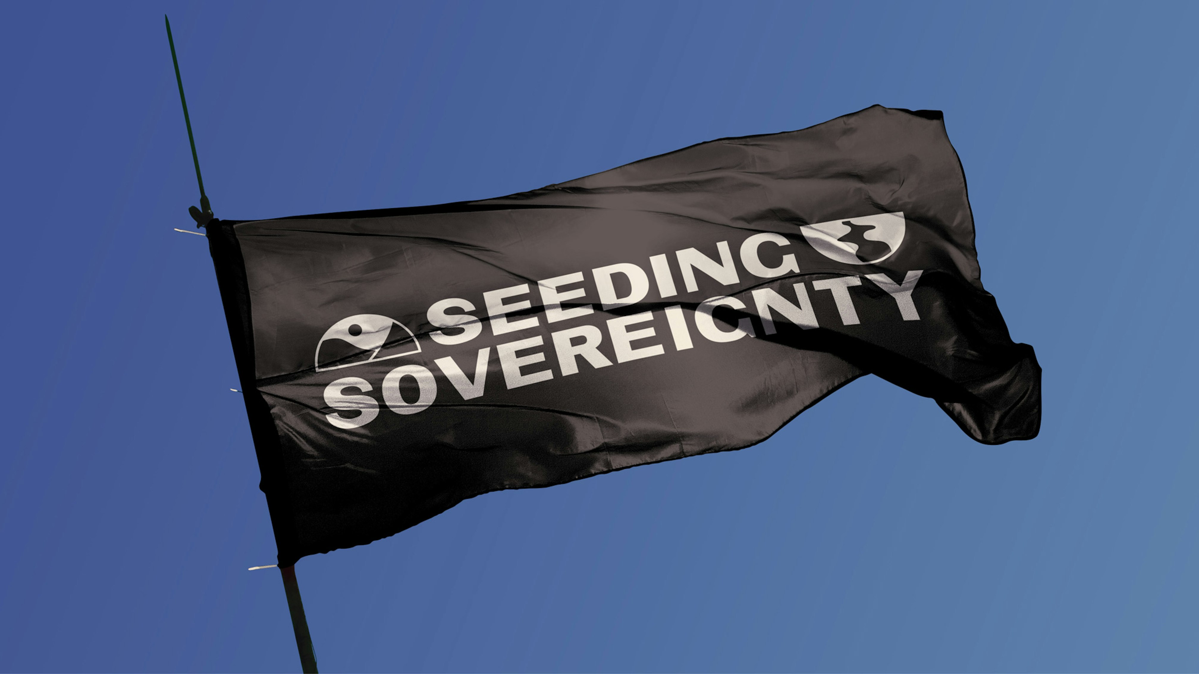 Image shows a black flag against a blue sky with the Seeding Sovereignty logo on it in white. 
