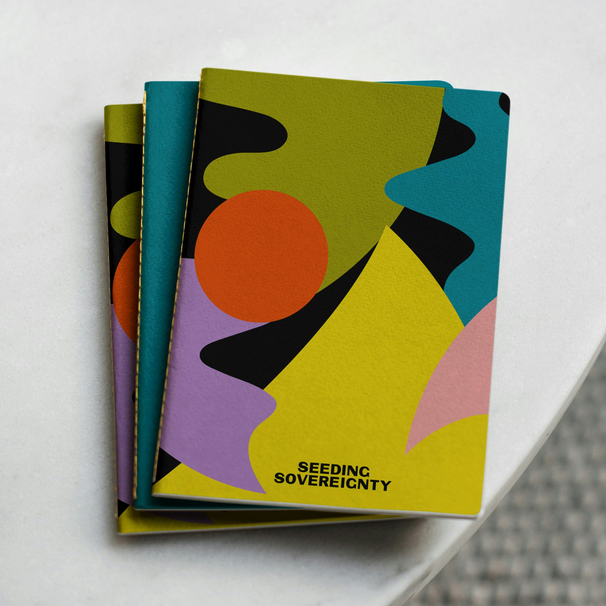 Image shows a stack of notebooks with multicolored abstract shapes on the covers.