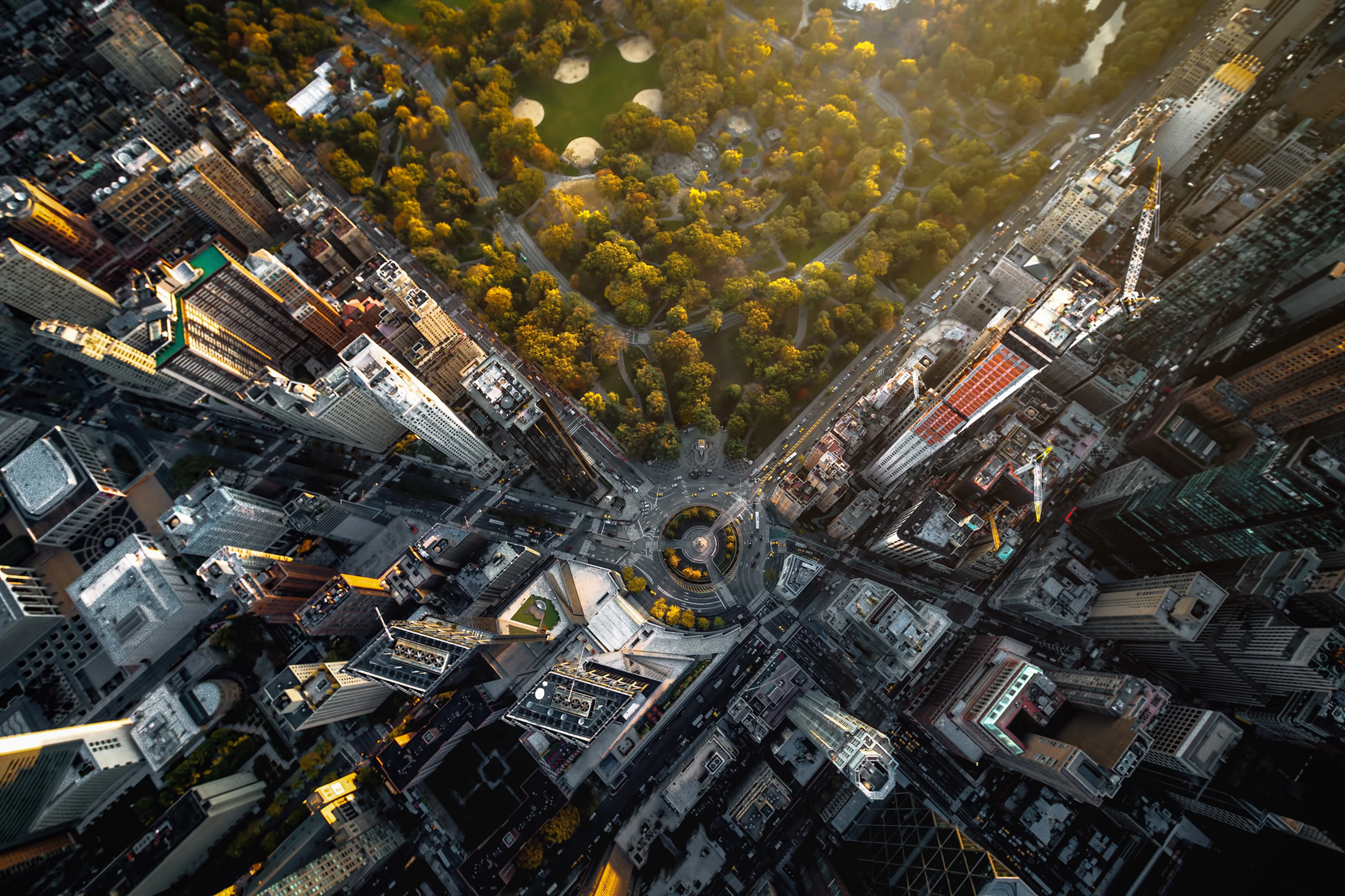 Photo taken from a helicopter flying above Manhatten. A corner of Central Park is in the upper middle part of the photo and surrounding it are highrisers.