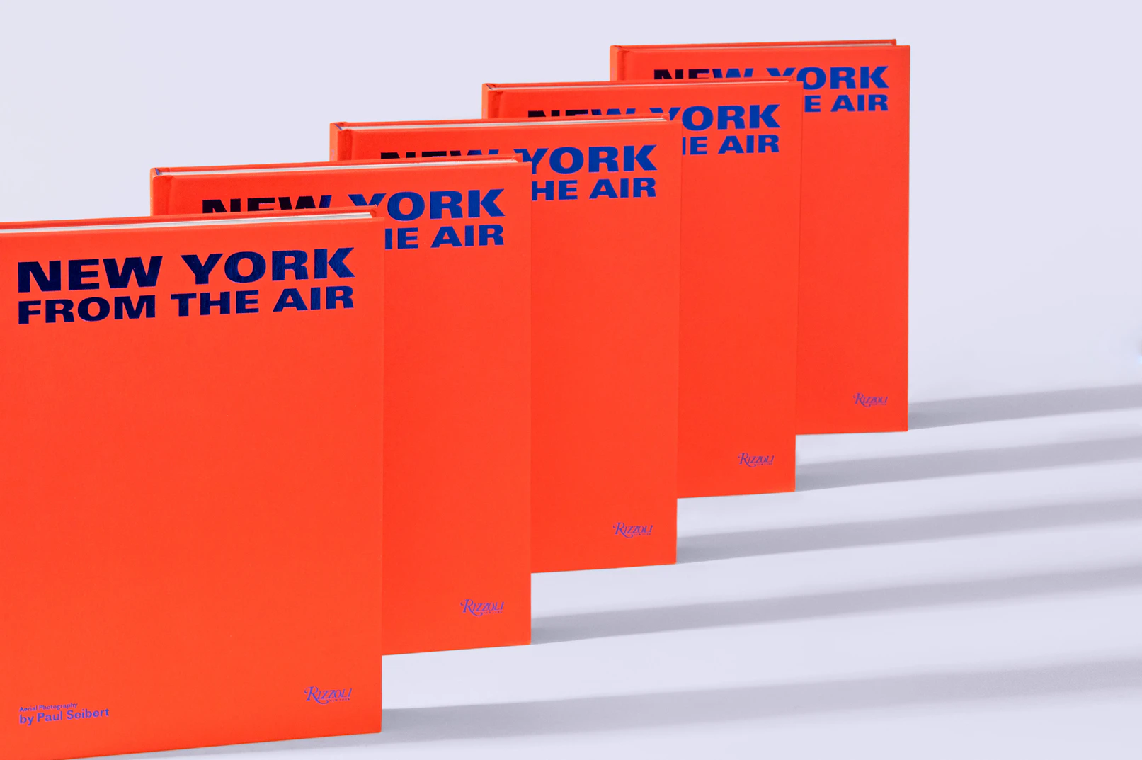 Photo of the red books with blue writing lined up behind each other forming a line on a gray seamless.