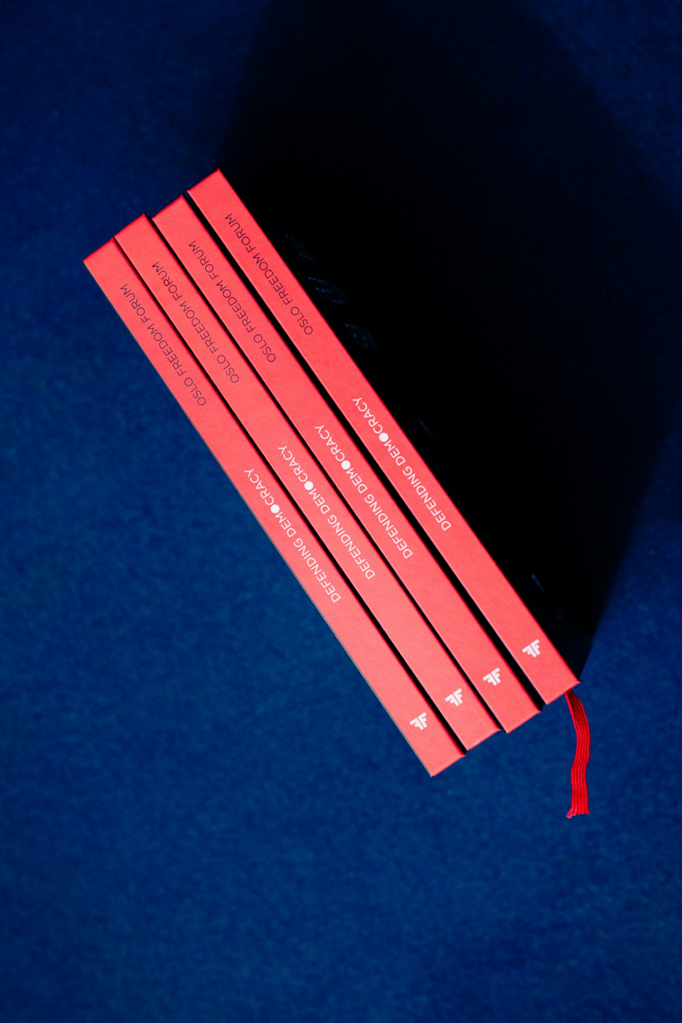 Image shows the coral-red spines of four books on a navy blue service.