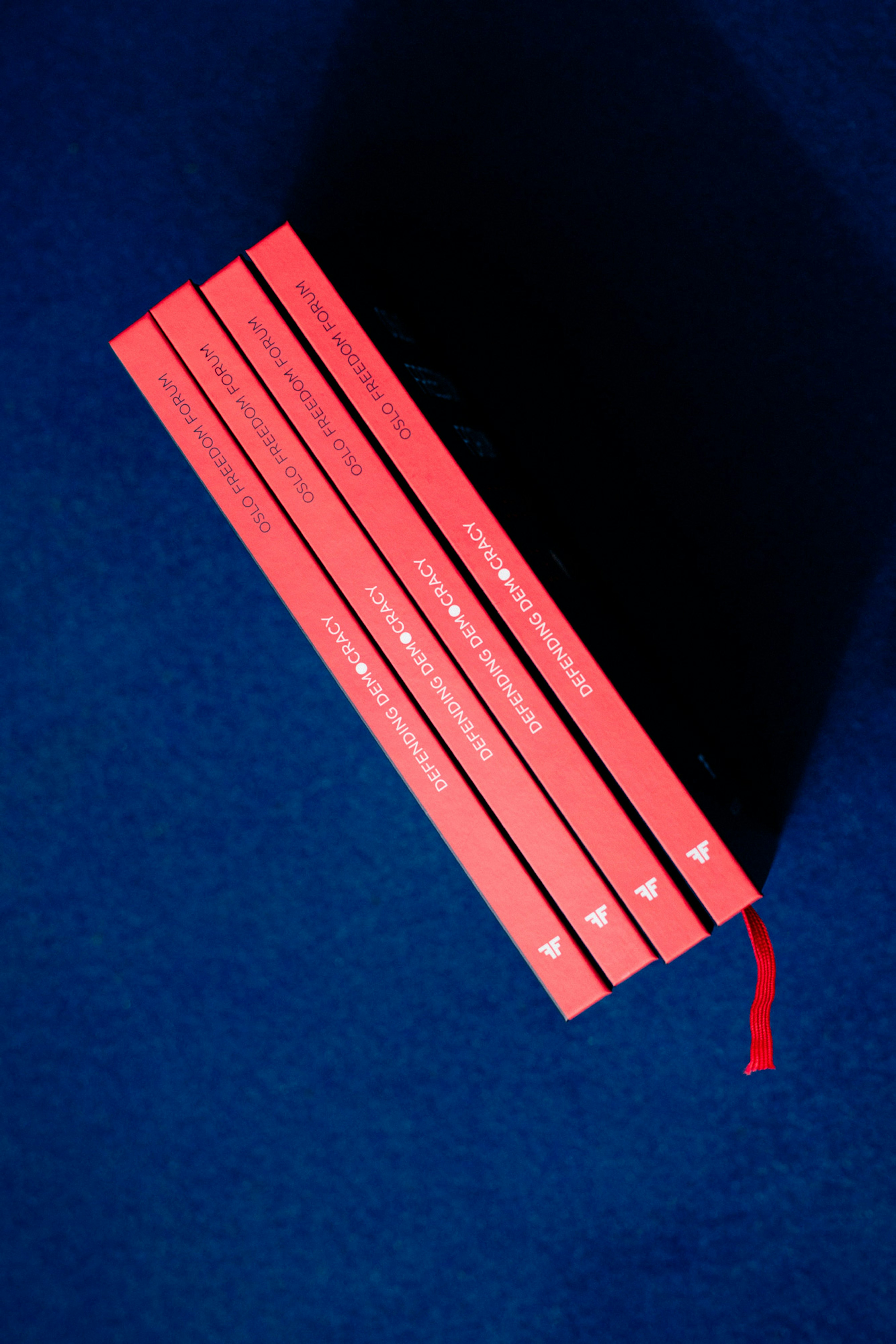 Image shows the coral-red spines of four books on a navy blue service. 