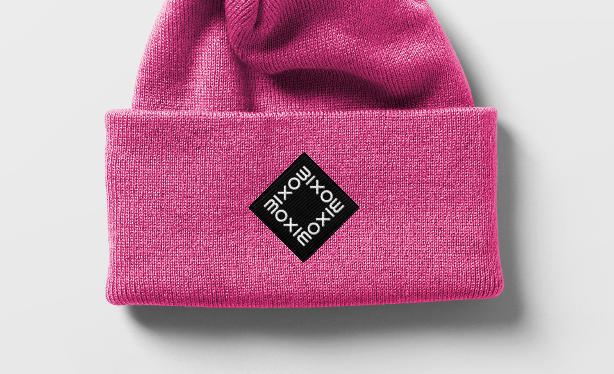 Moxie Beanie in pink with the wordmark in a square in white on a black diamond square.