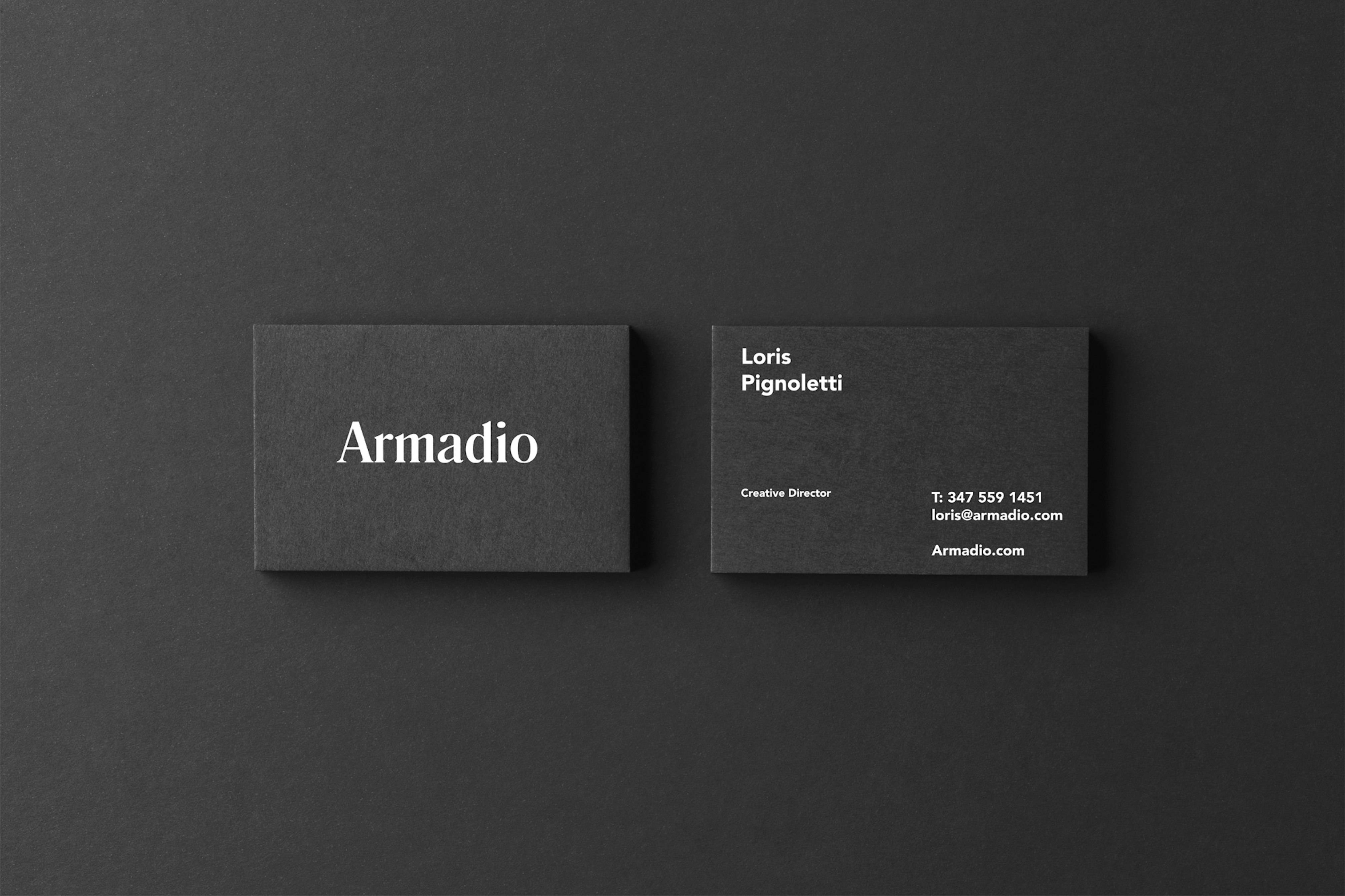 Image shows the front and back of a charcoal gray business card on a same-color background. The front reads Armadio and the back shows the employee information in white text. 