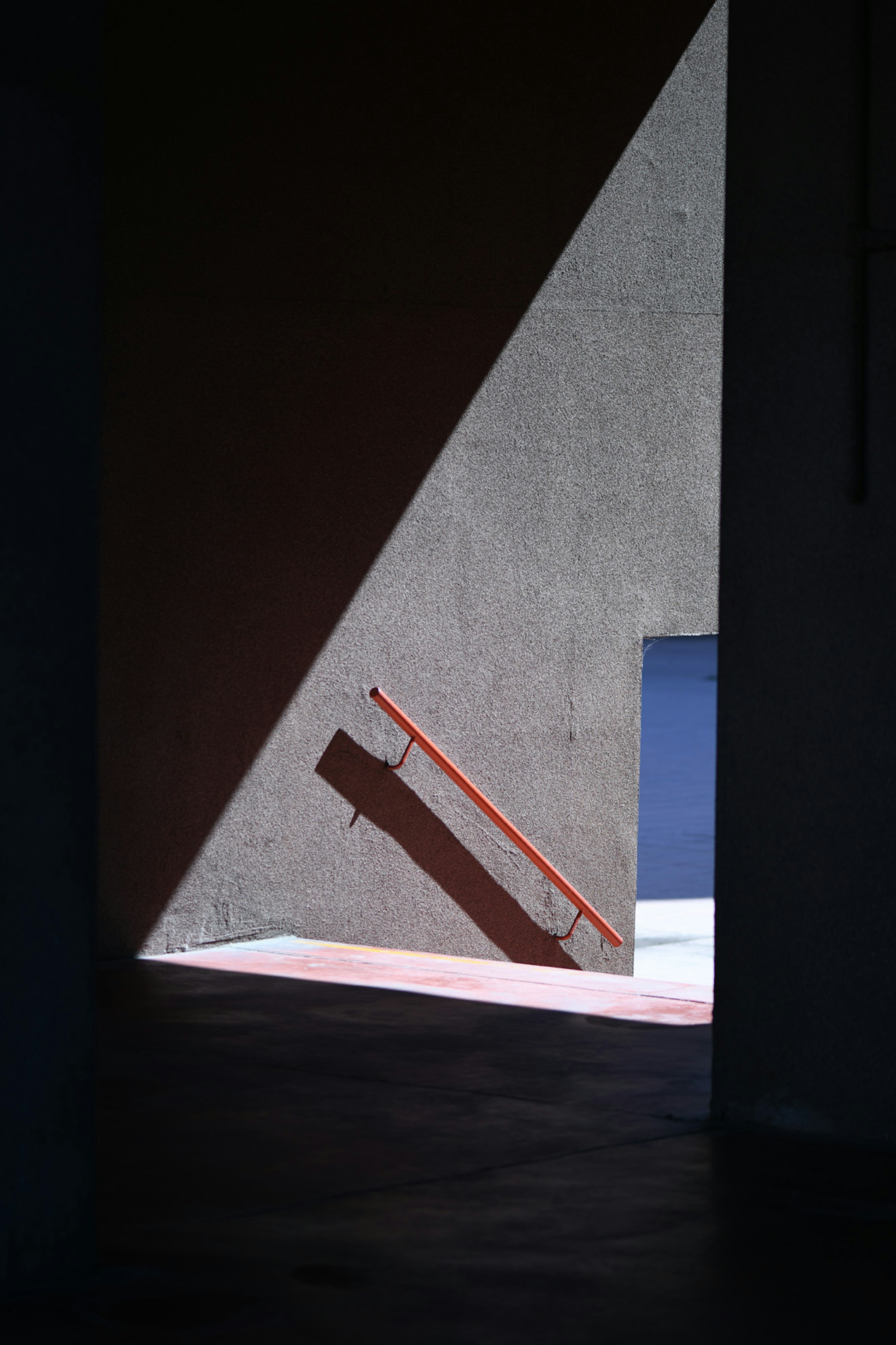 Photo showing an outdoors staircase with a red handle. In the background there is a blue door.