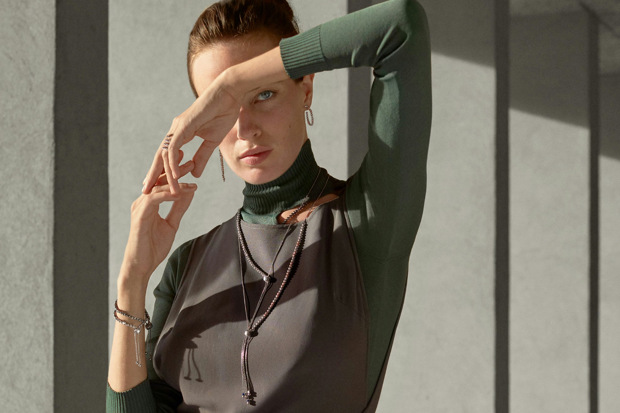 Image of person standing against outdoors architectural details. They are wearing a combo of green and gray clothes as well as the product.