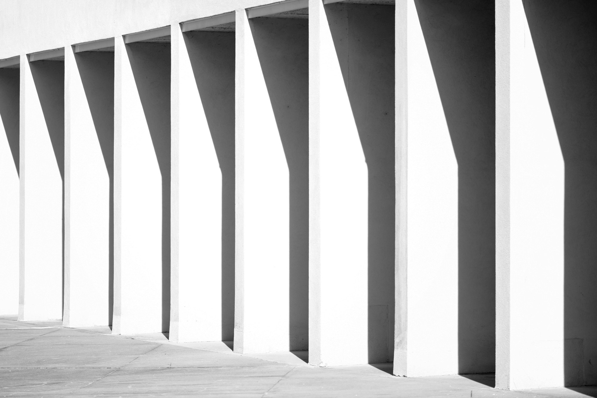 Photo showing outdoor architectural details of white columns with strong shadows on them.