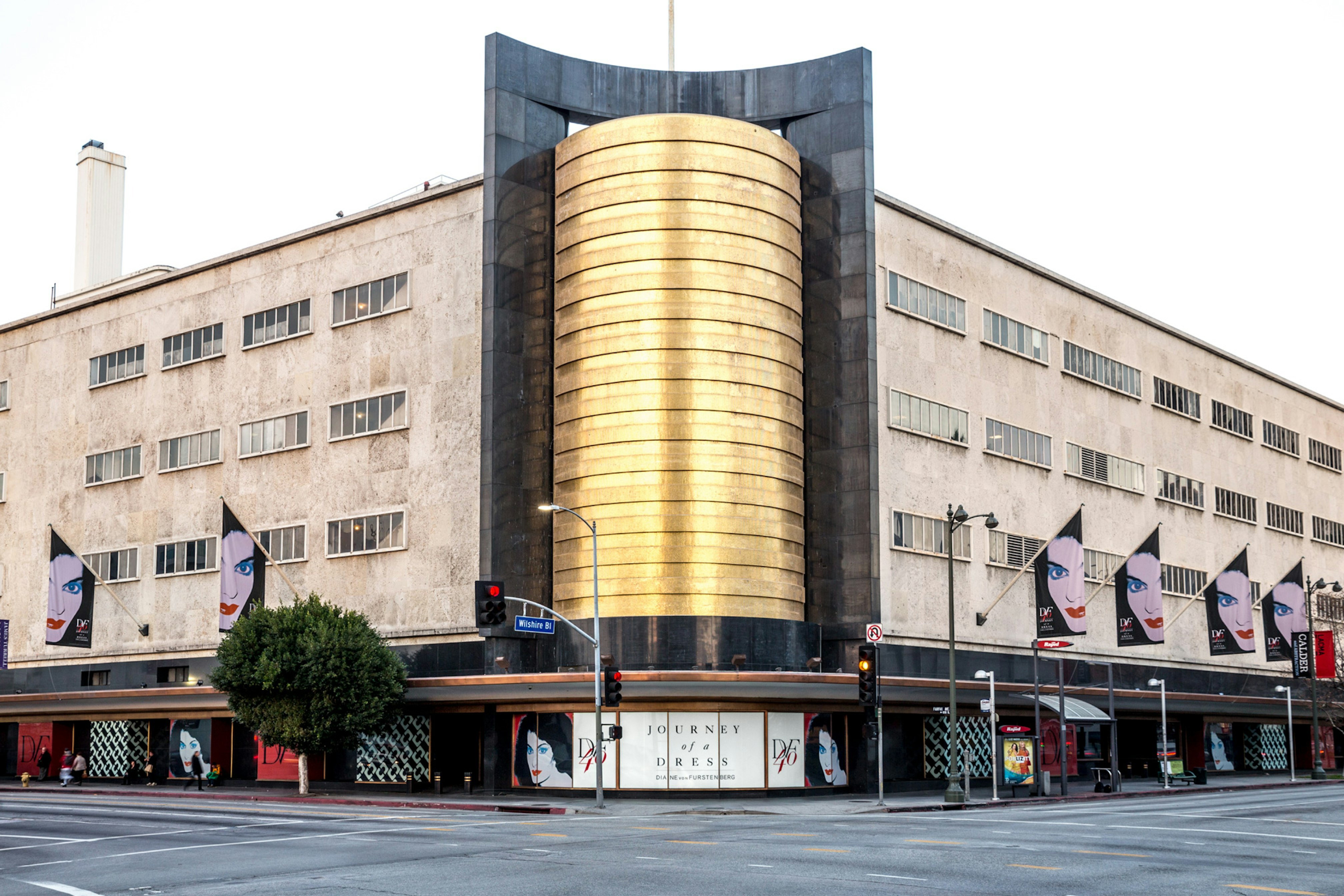 Image showing the outside of the LACMA building. The corner has a tall gold column and on both sides of the building there are flags showing the face of Diane Von Furstenberg.