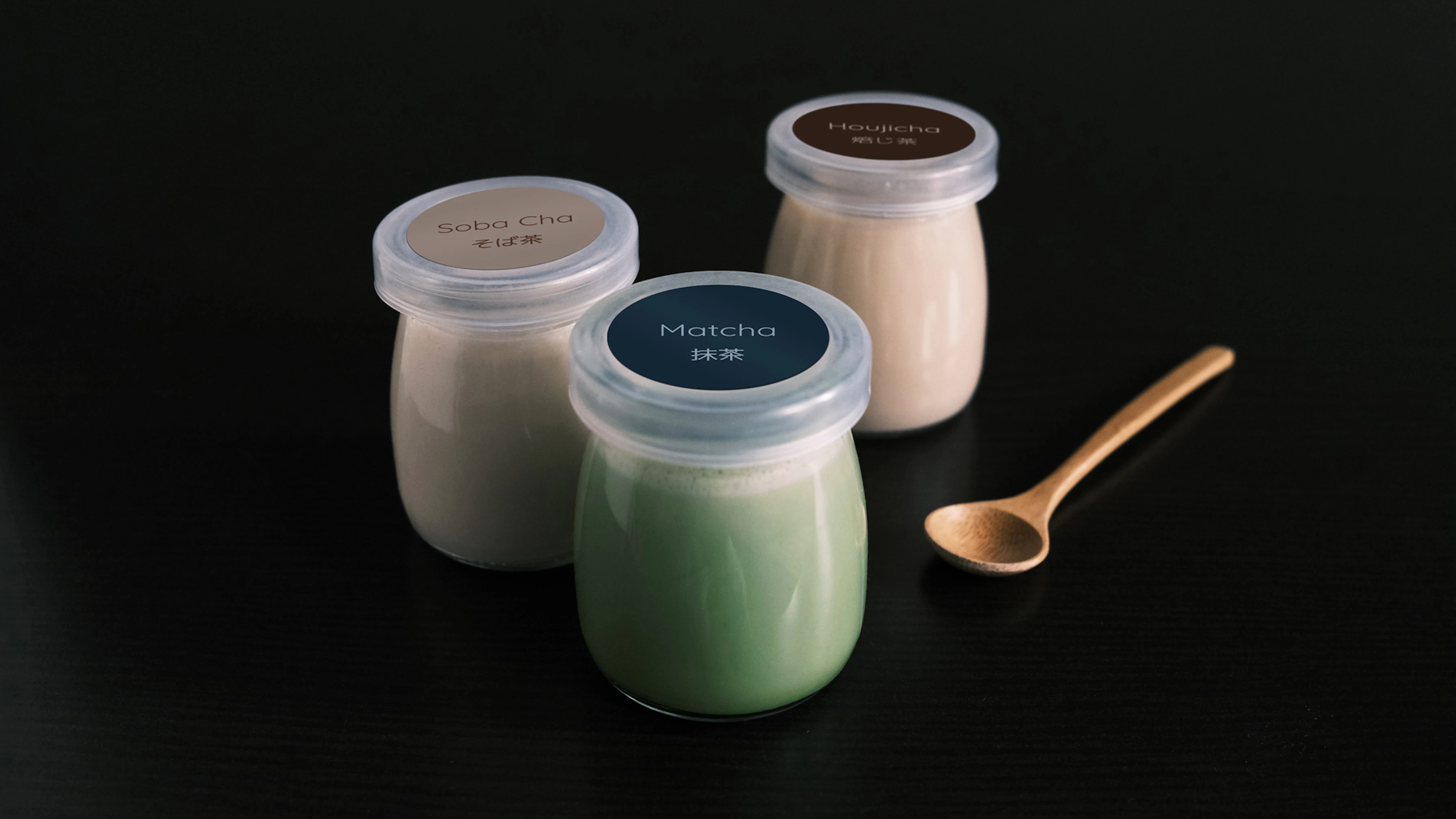 Image showing three little pots filled with Kettl pudding. A wooden spoon is next to them and everything is on a black background.