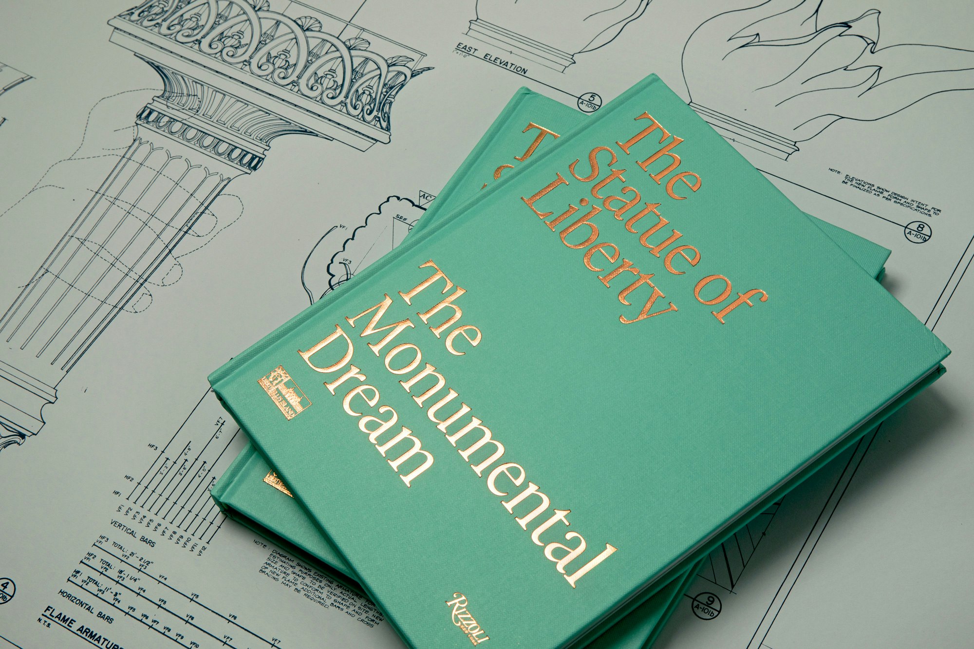 Image showing a stack of two of the green books on top of each other resting on a gray poster with the blue print of the torch printed on top.