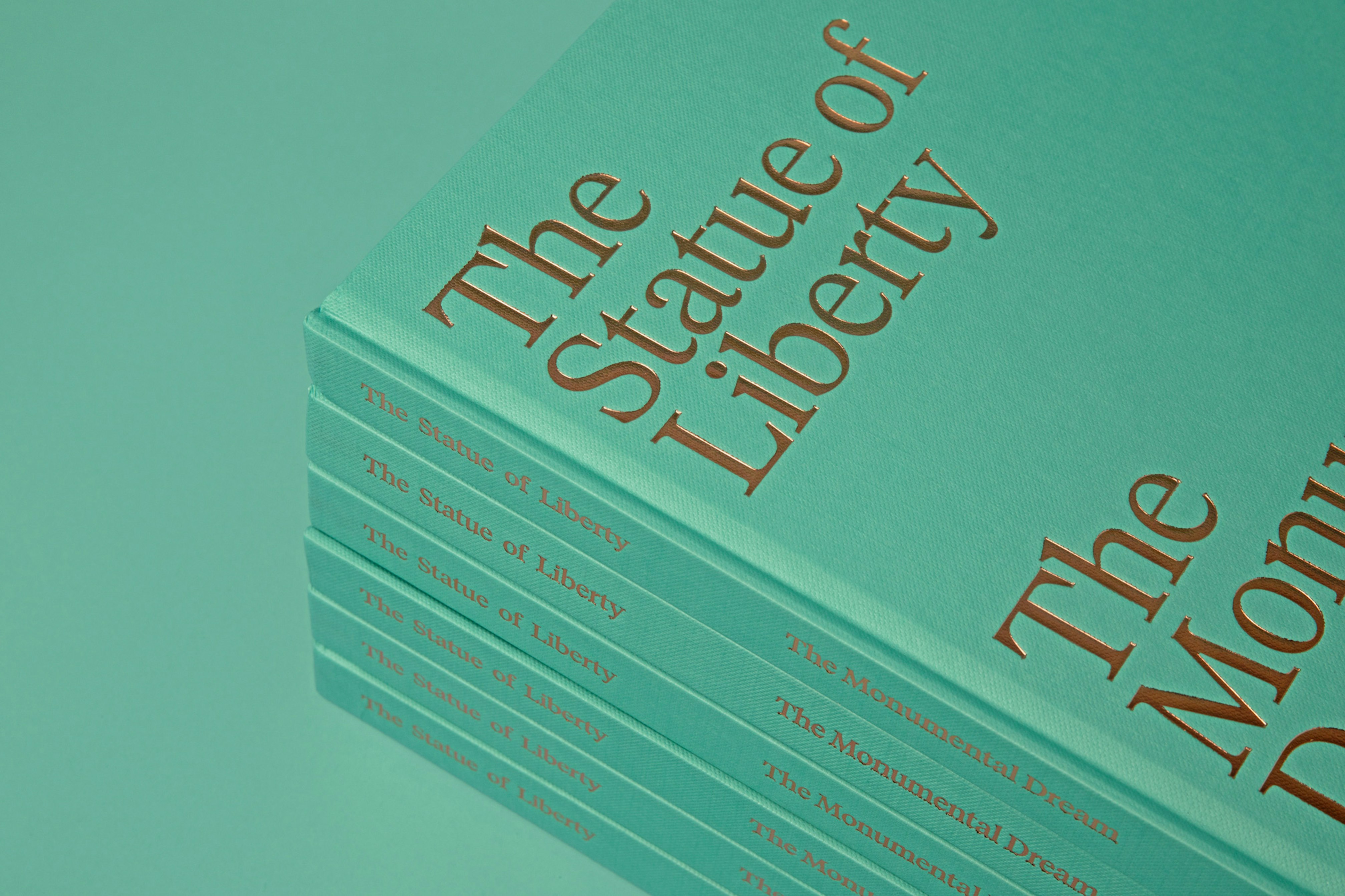 Image showing close up of a stack of the green books saying THE STATUE OF LIBERTY on the cover printed in copper. The stack is resting on a green background.