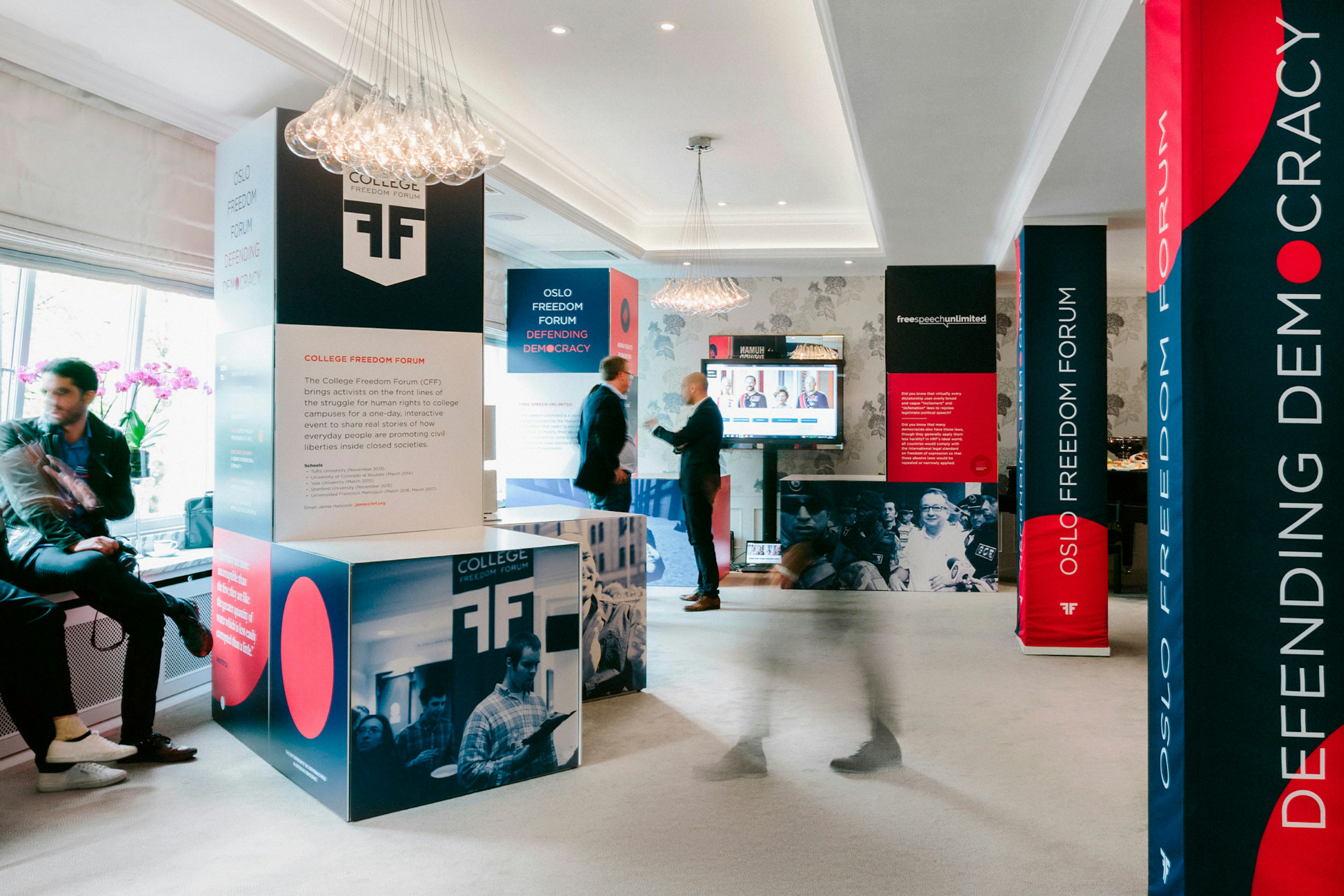 Image shows 3D Oslo Freedom Forum installations in a room where people are talking and walking around. 