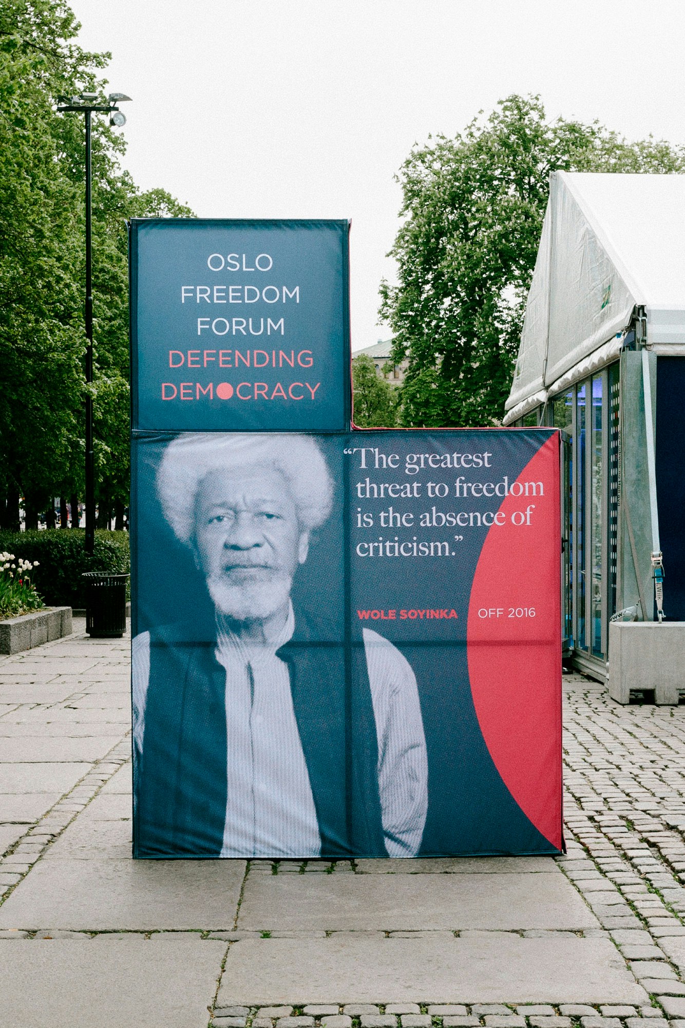 Image shows a 3D installation created using 5 cube in an L-shape. It shows a blue-toned image of a person and says "OSLO FREEDOM FORUM DEFENDING DEMOCRACY," and "The greatest threat to freedom is the absence of criticism."