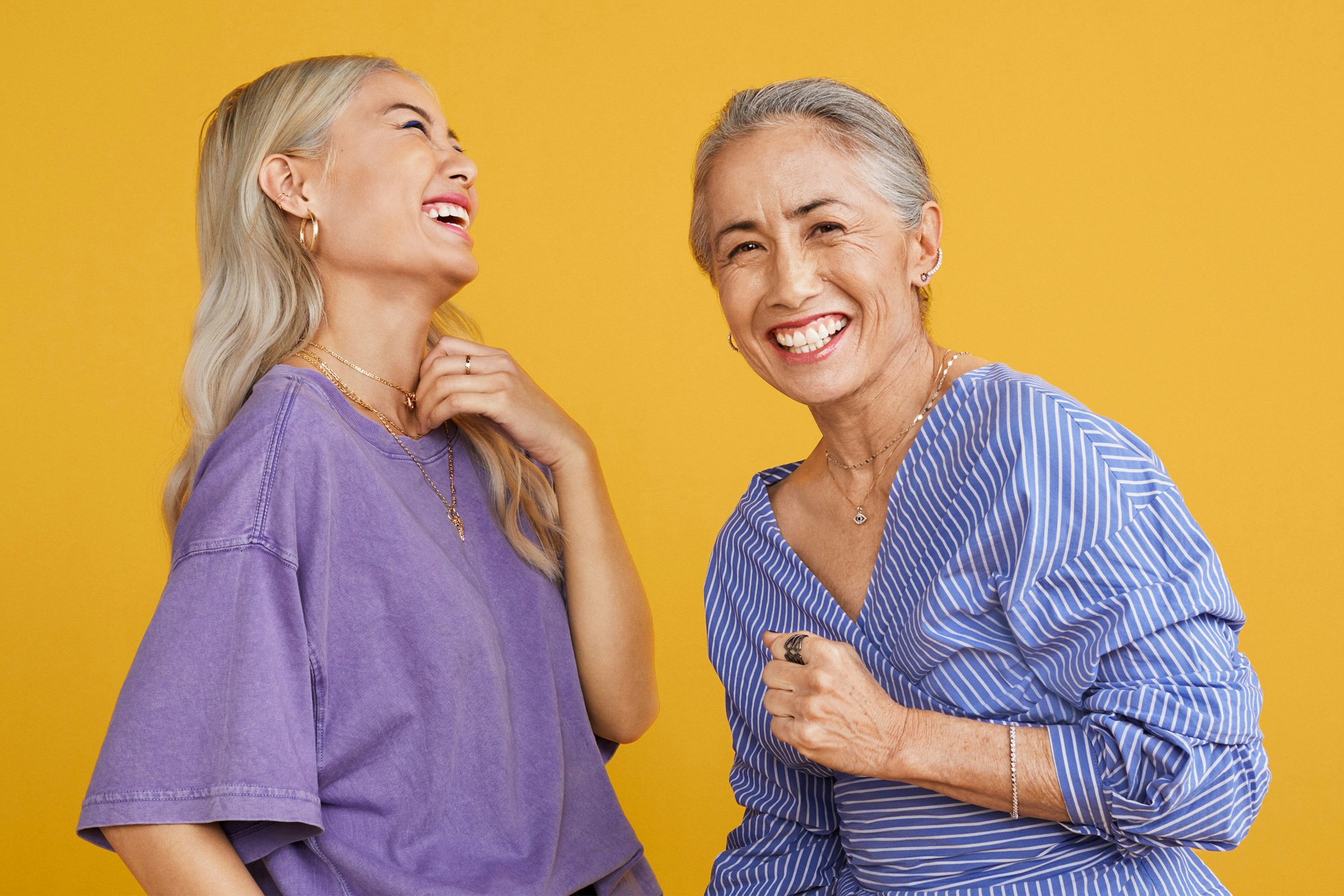 Image showing two people standing in front of a warm yellow seamless. They are both laughing. One is wearing a purple teeshirt and the other a blue shirt with white stripes.