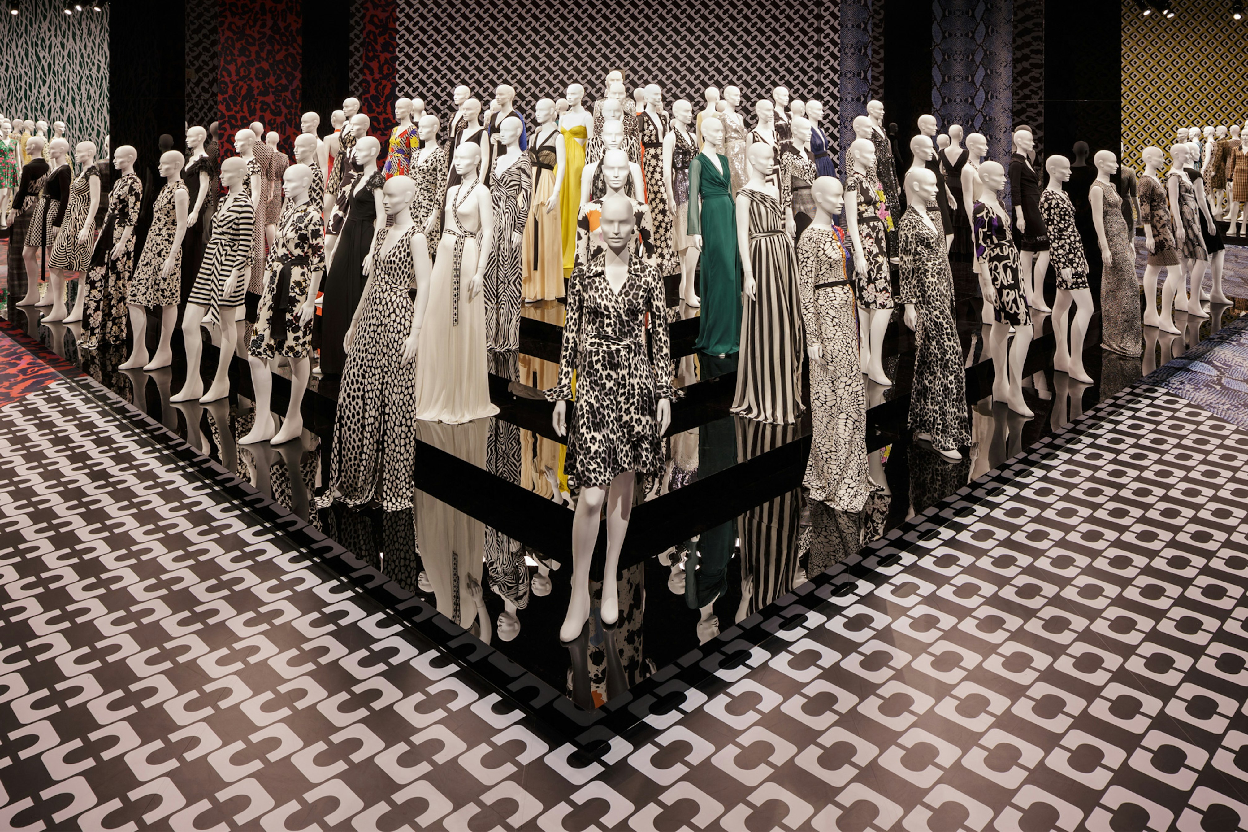 Image showing one of the rooms inside LACMA. There are a lot of mannequins standing in rows and lines, each wearing a different DVF wrap dress. On the floor is one of DVFs classic prints.