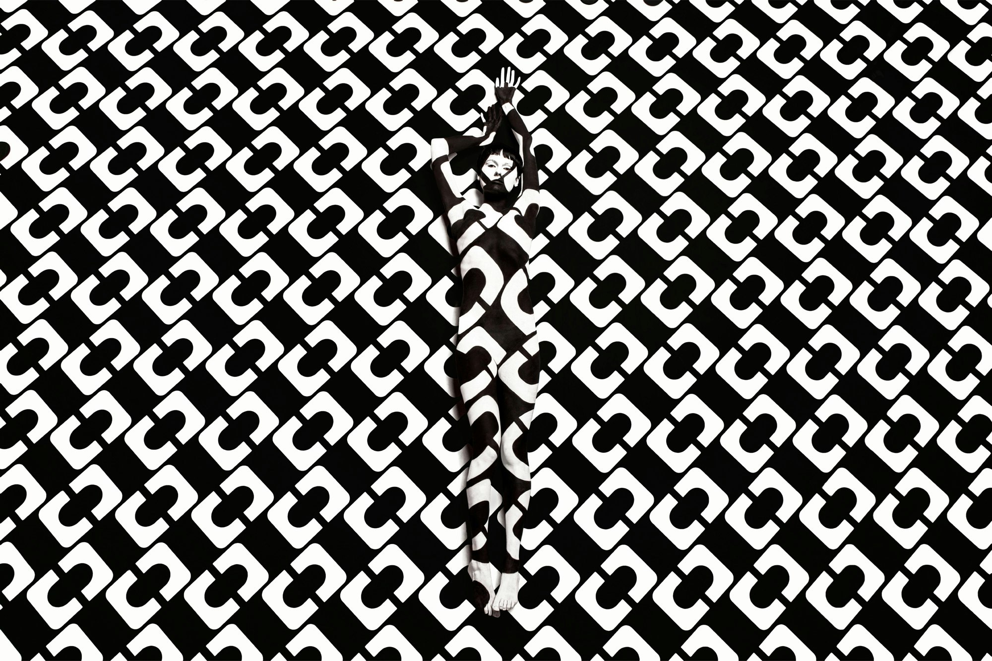 Image showing person against a black white DVF print. Their body is painted in the same print making a camouflage effect.