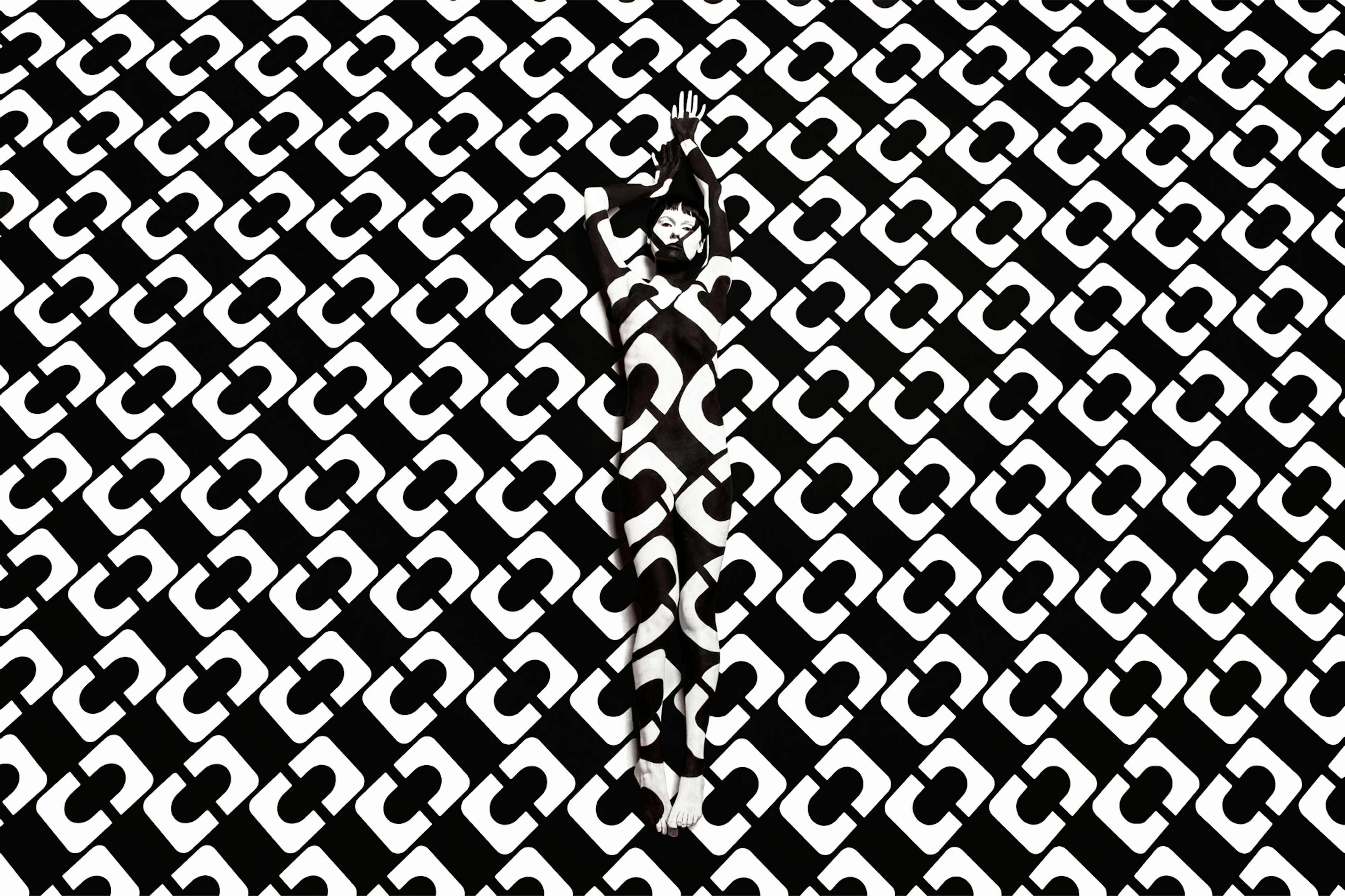 Image showing person against a black white DVF print. Their body is painted in the same print making a camouflage effect.