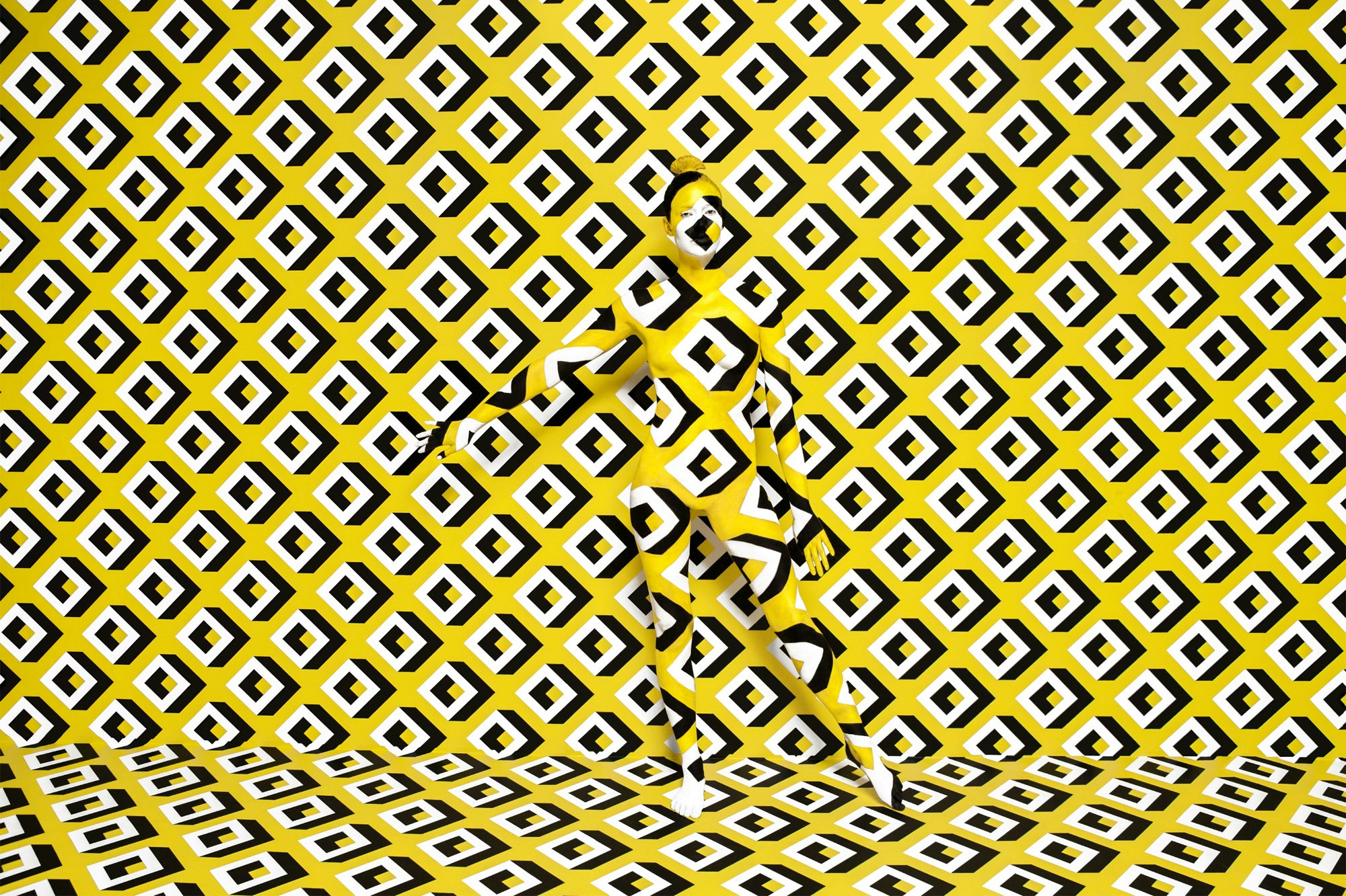 Image showing a wall and floor covered in DVFs yellow print. In front is a person standing who is painted in the same print.