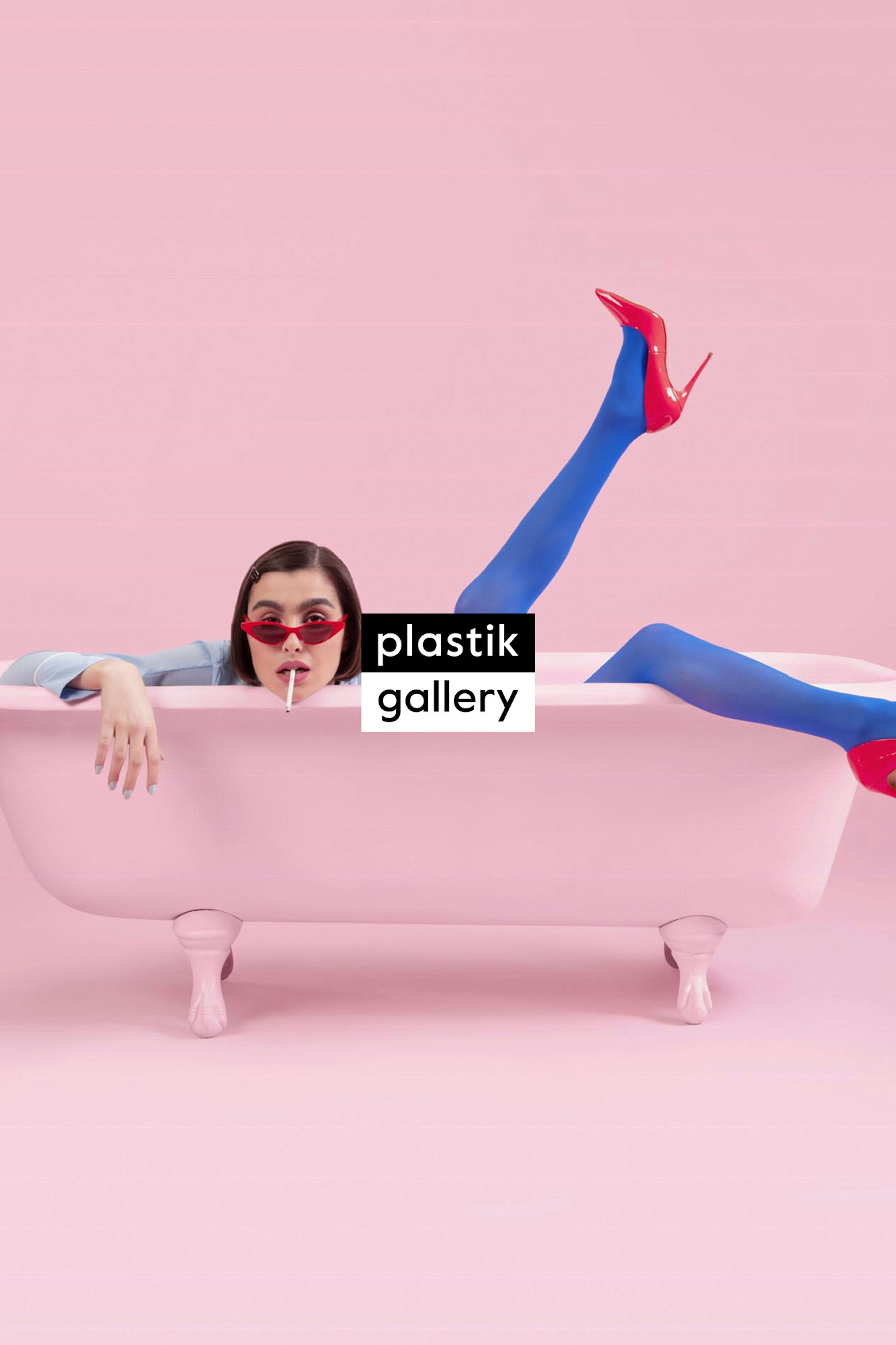 Image shows the plastik gallery logo in black and white on top of an image of a person in a pink tub on a pink background. The person has brown hair that is parted on the site. They are wearing bright blue tights with bright red heels with one foot in the air. They have on bright red sunglasses and have a lollipop in their mouth.