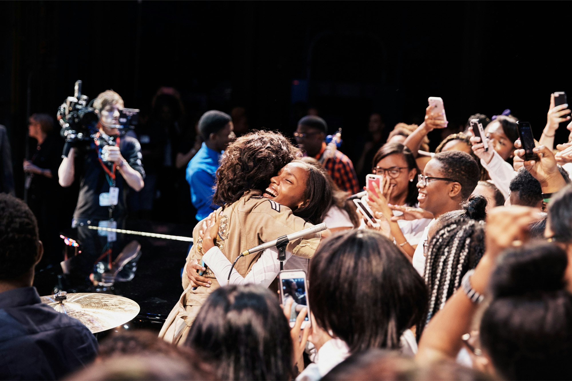 Image shows a person in a crowd smiling big with their eyes closed, hugging Alicia Keys. Others in the crowd take photos with their phones.