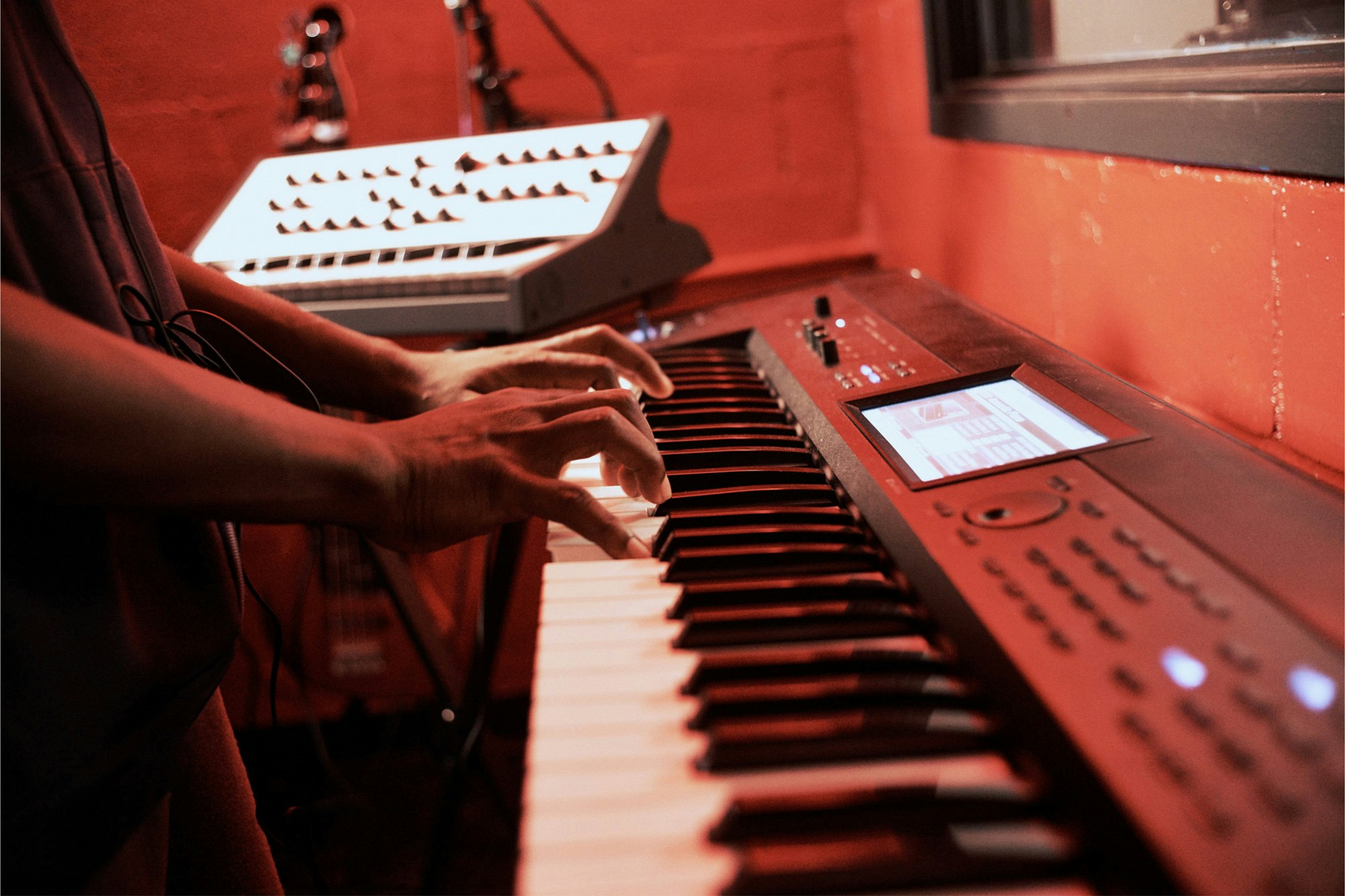 Image shows a close-up of a persons hands playing a keyboard in a red-lit room.