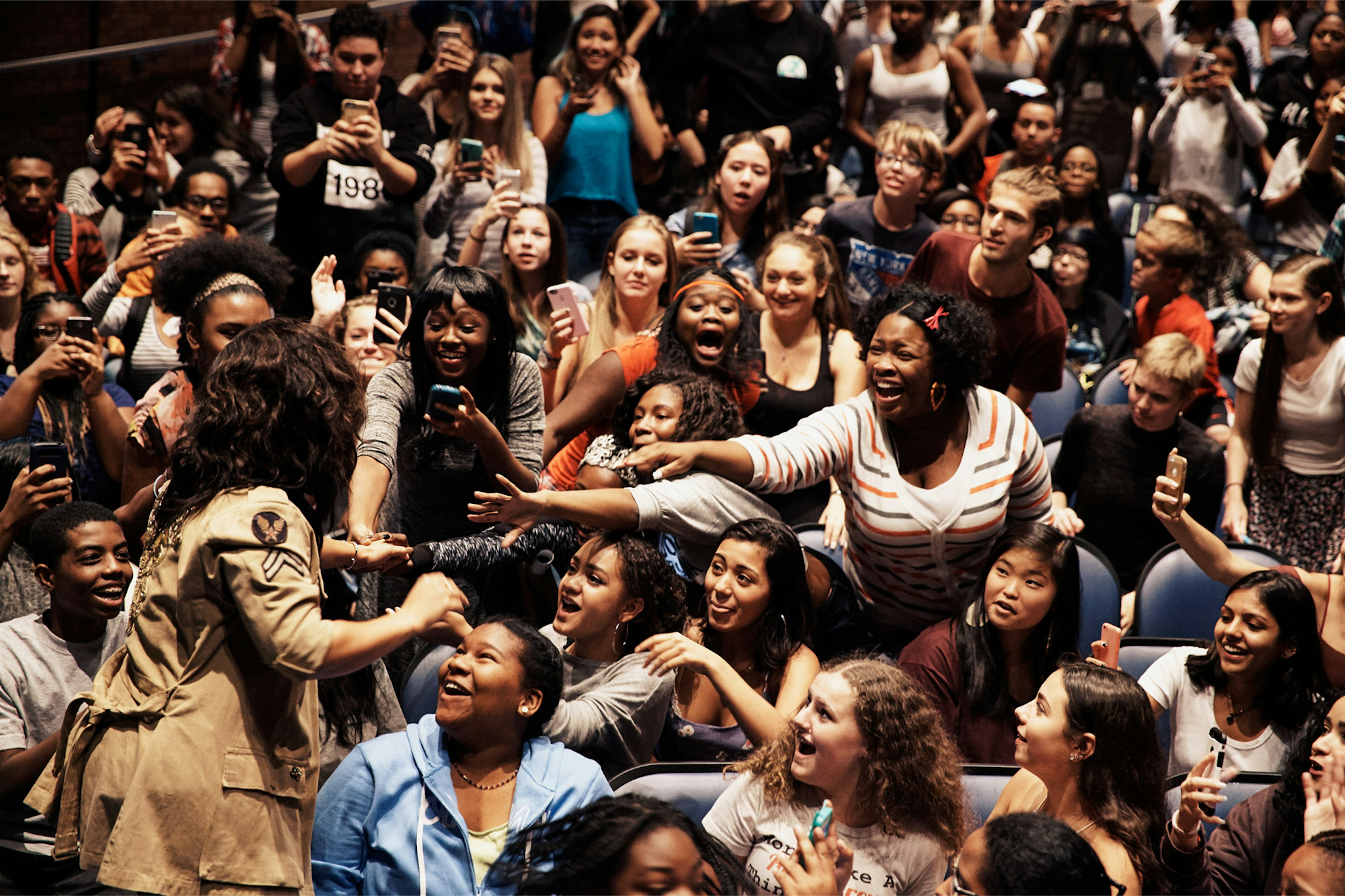 Image shows a crowd of people screaming, laughing, and taking photos as Alicia Keys leans over them and greets them. 